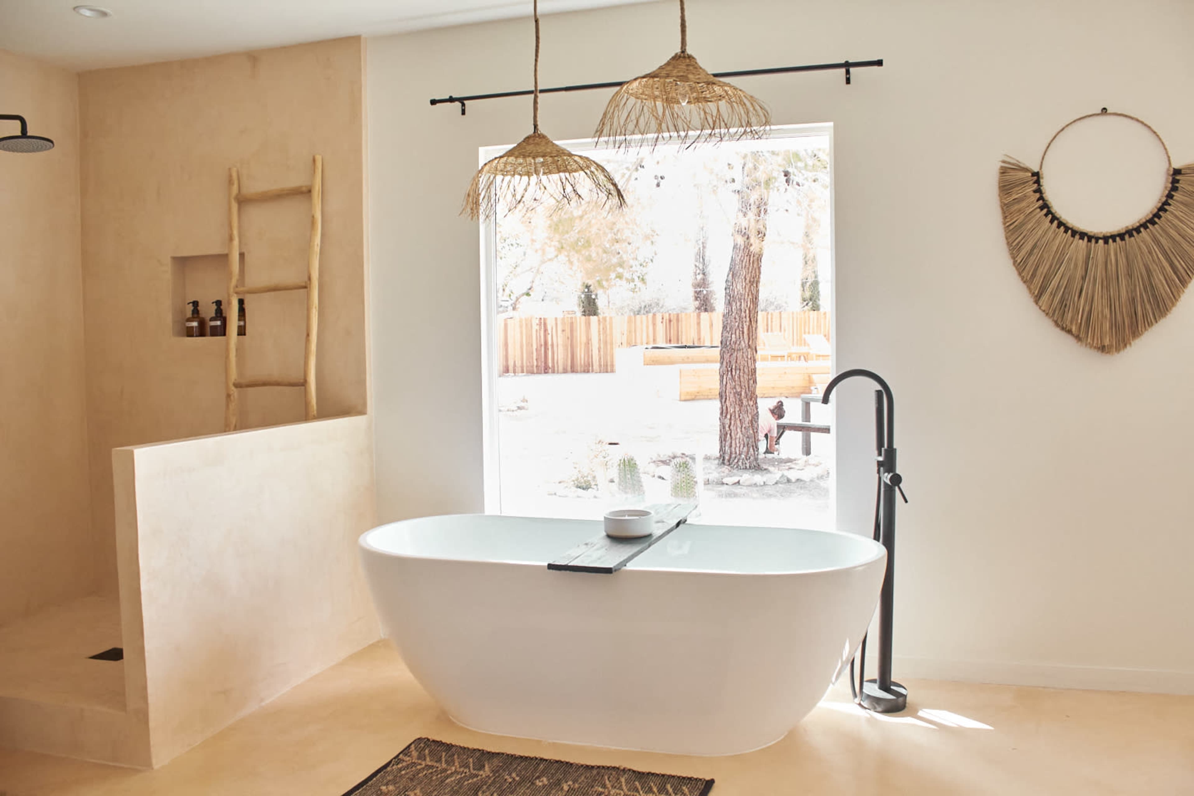 The image features a modern bathroom with a freestanding bathtub, natural elements like woven decor, and a large window overlooking an outdoor area.