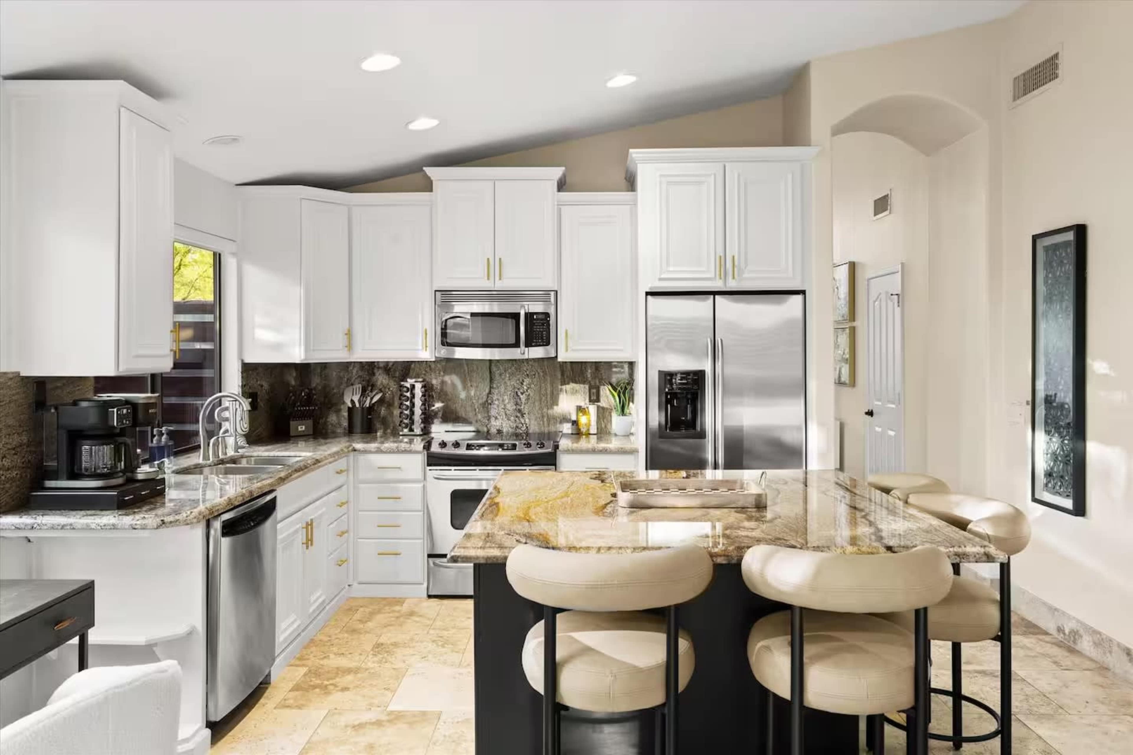 The image shows a modern kitchen with white cabinetry, stainless steel appliances, and a large island with bar seating.