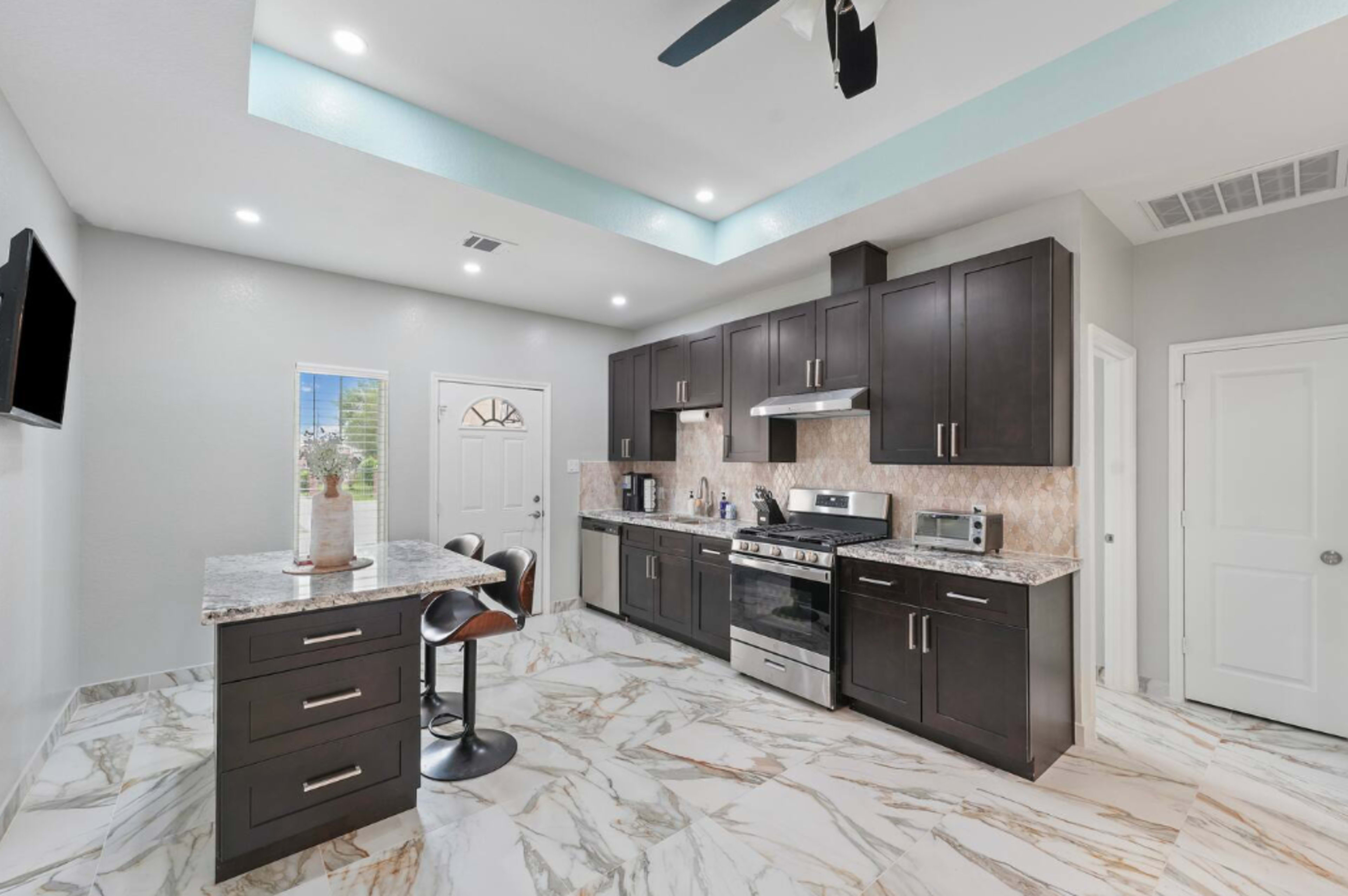 The image shows a modern kitchen featuring dark wood cabinetry, stainless steel appliances, and marble flooring.