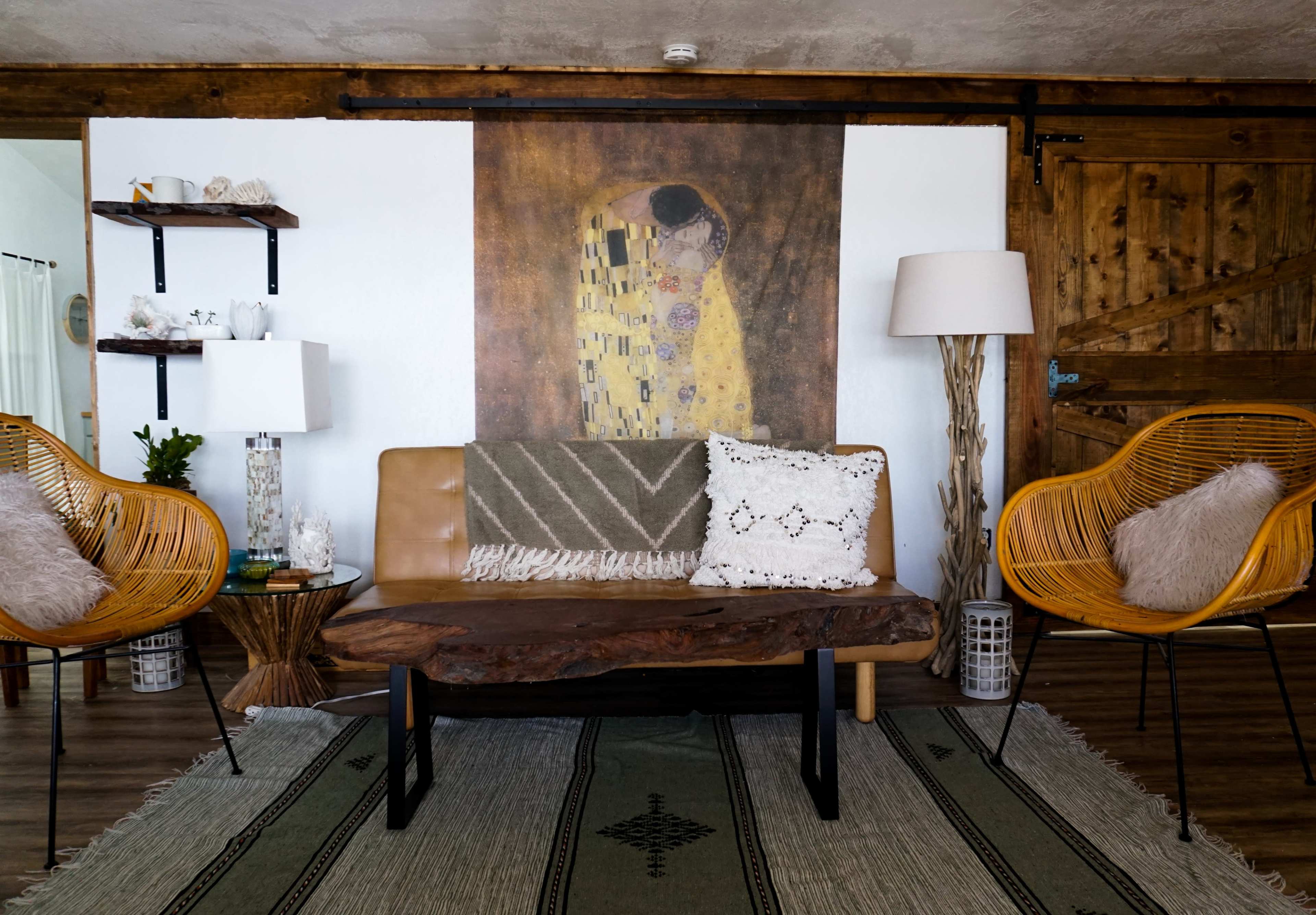 The scene features a living room with a leather sofa, two woven chairs, a large decorative wall art piece, and a patterned rug.
