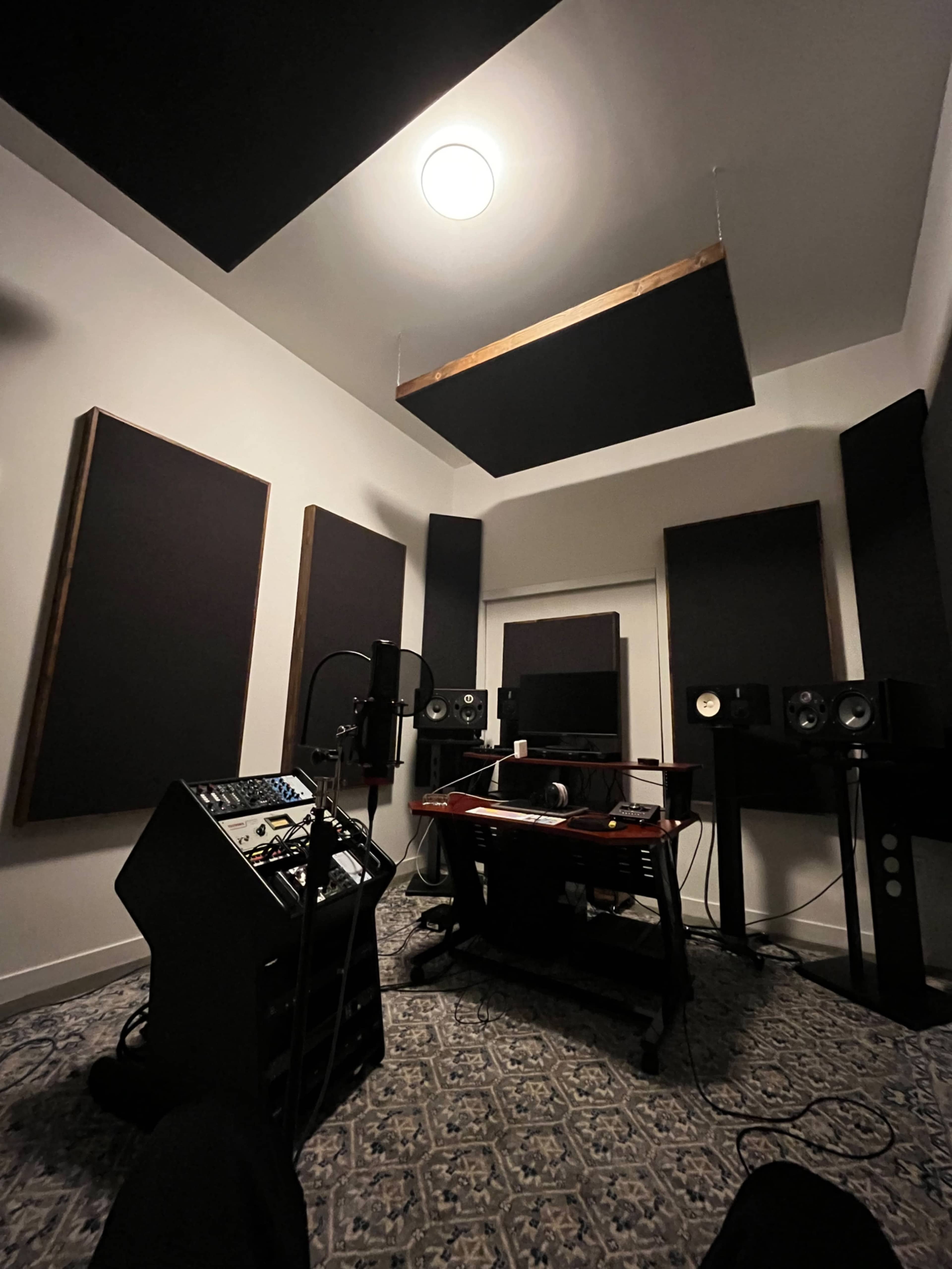 The image shows a recording studio with soundproofed walls, audio equipment, and a central mixing desk.