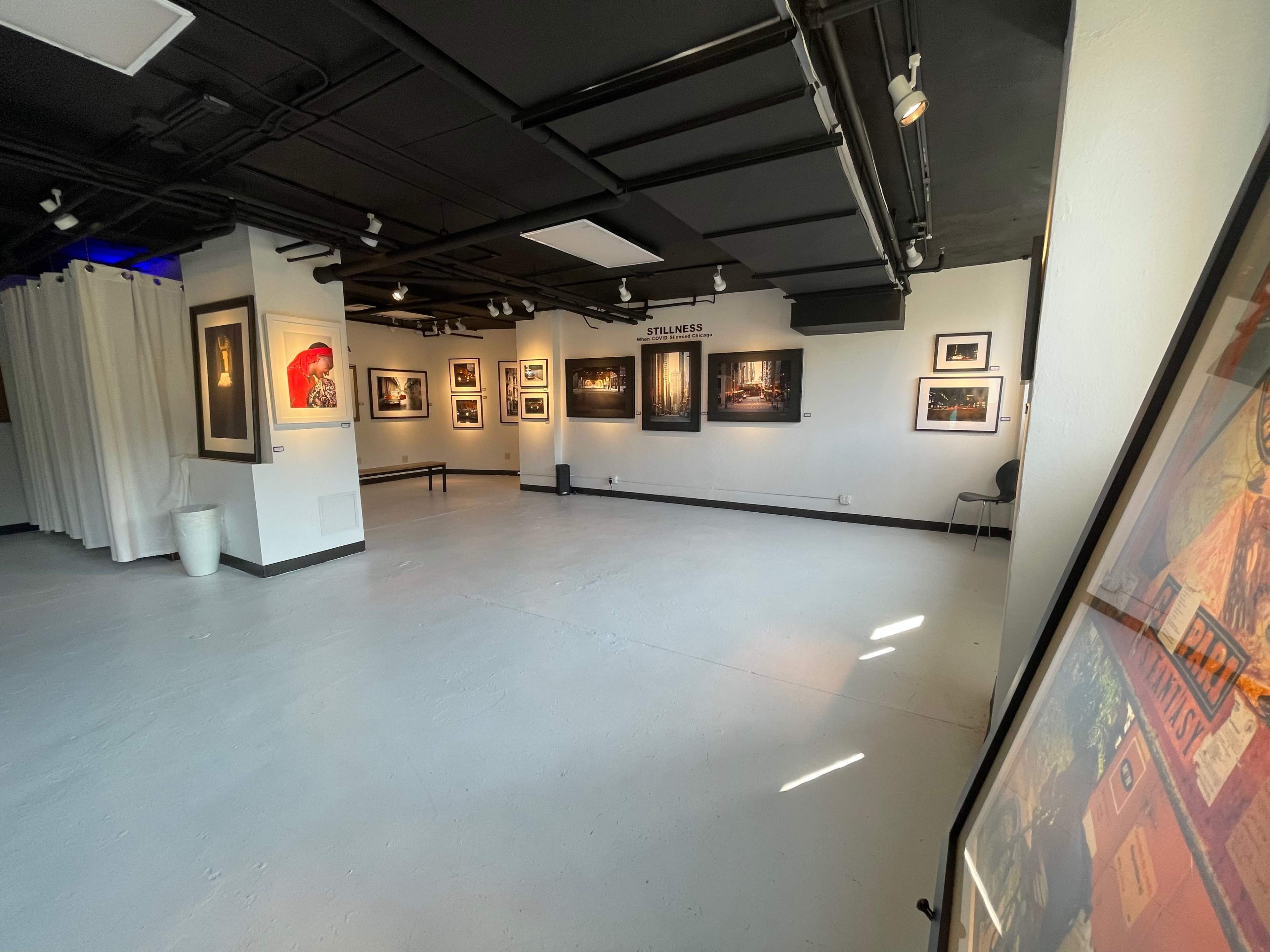 An interior view of an art gallery featuring framed photographs on white walls, with a polished concrete floor and minimalistic furniture.
