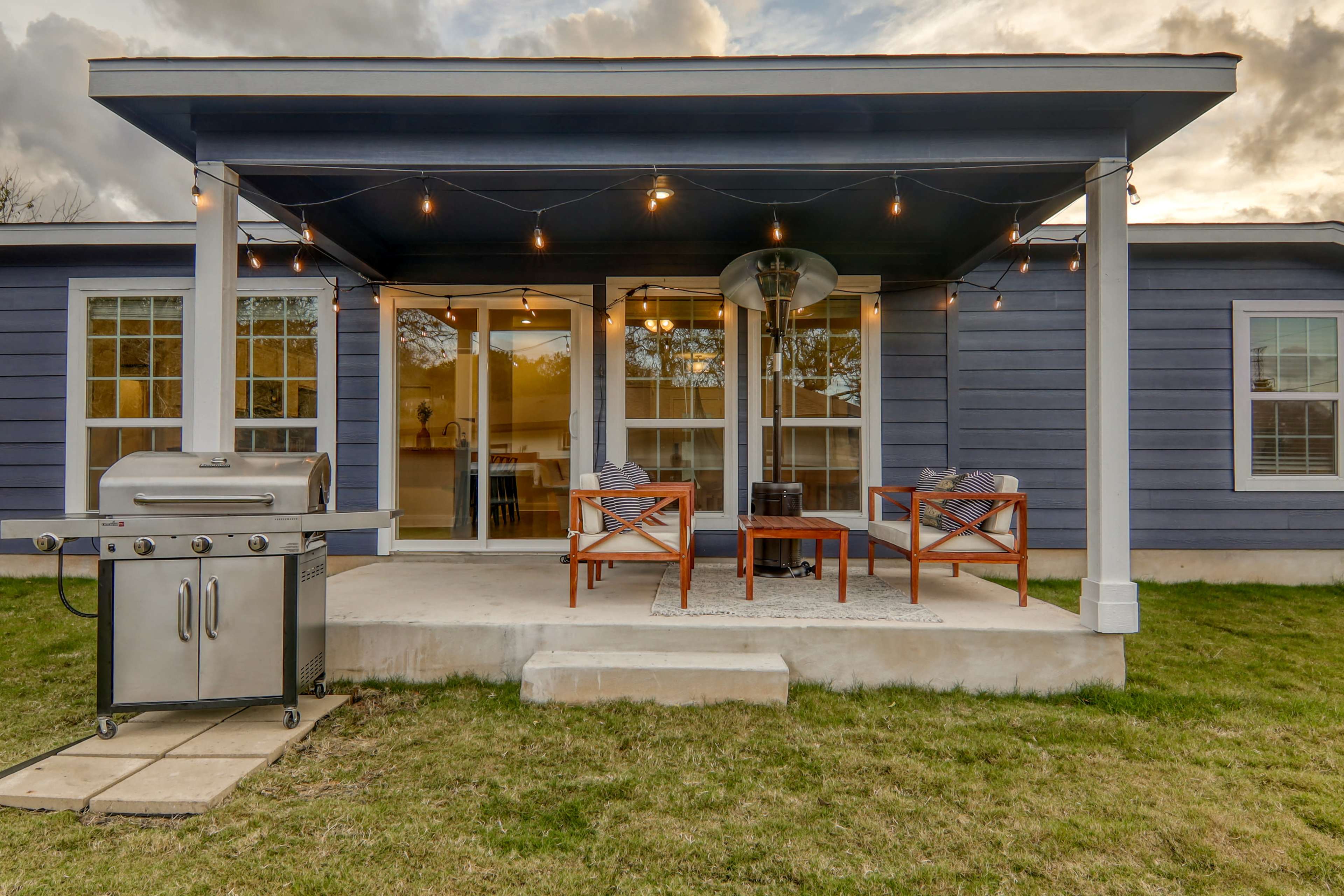 A back patio features a gas grill, two chairs, and a small table under a covered area with string lights.