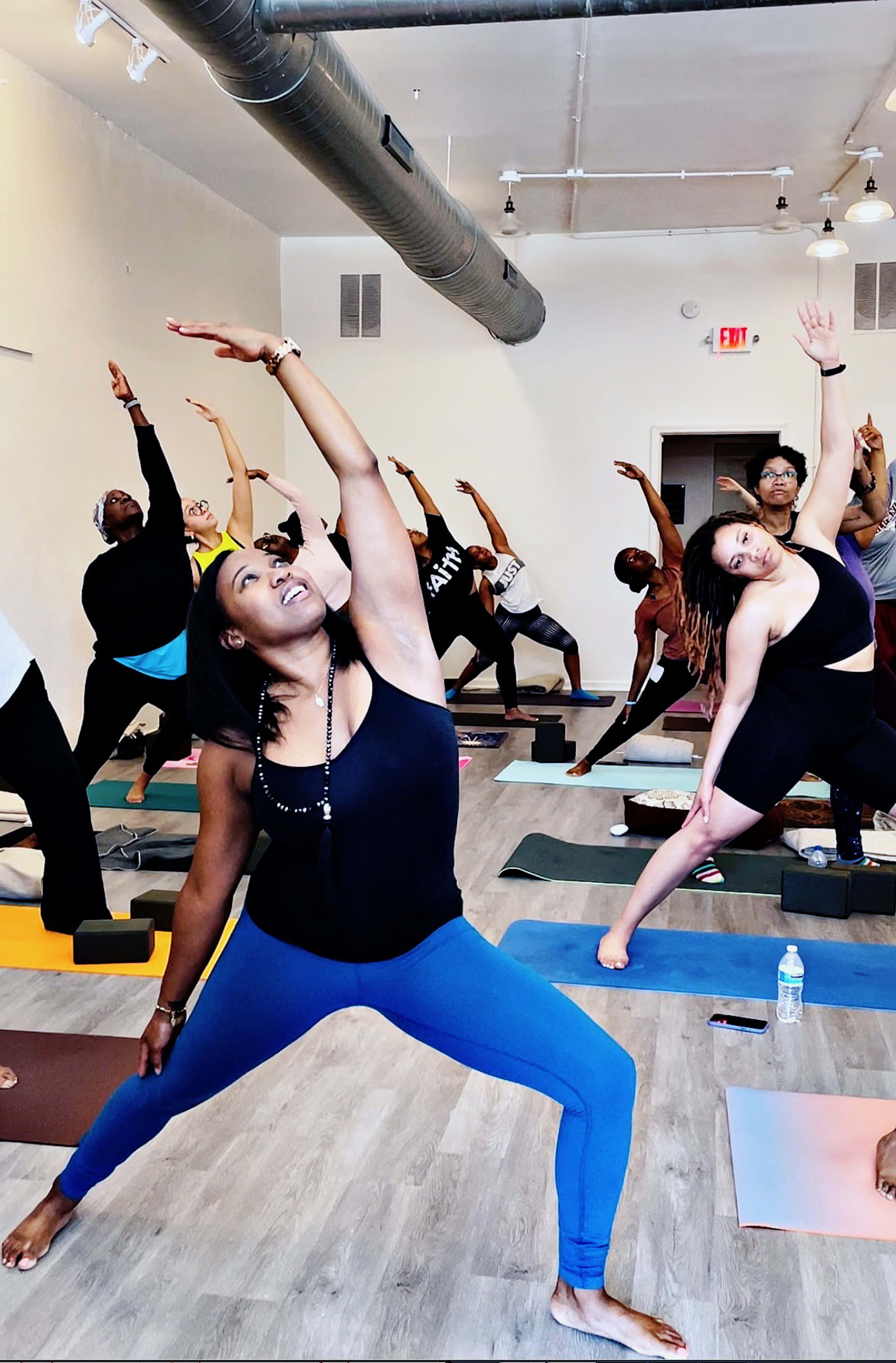 A group of people practices yoga in a studio, each performing various stretching poses on yoga mats.