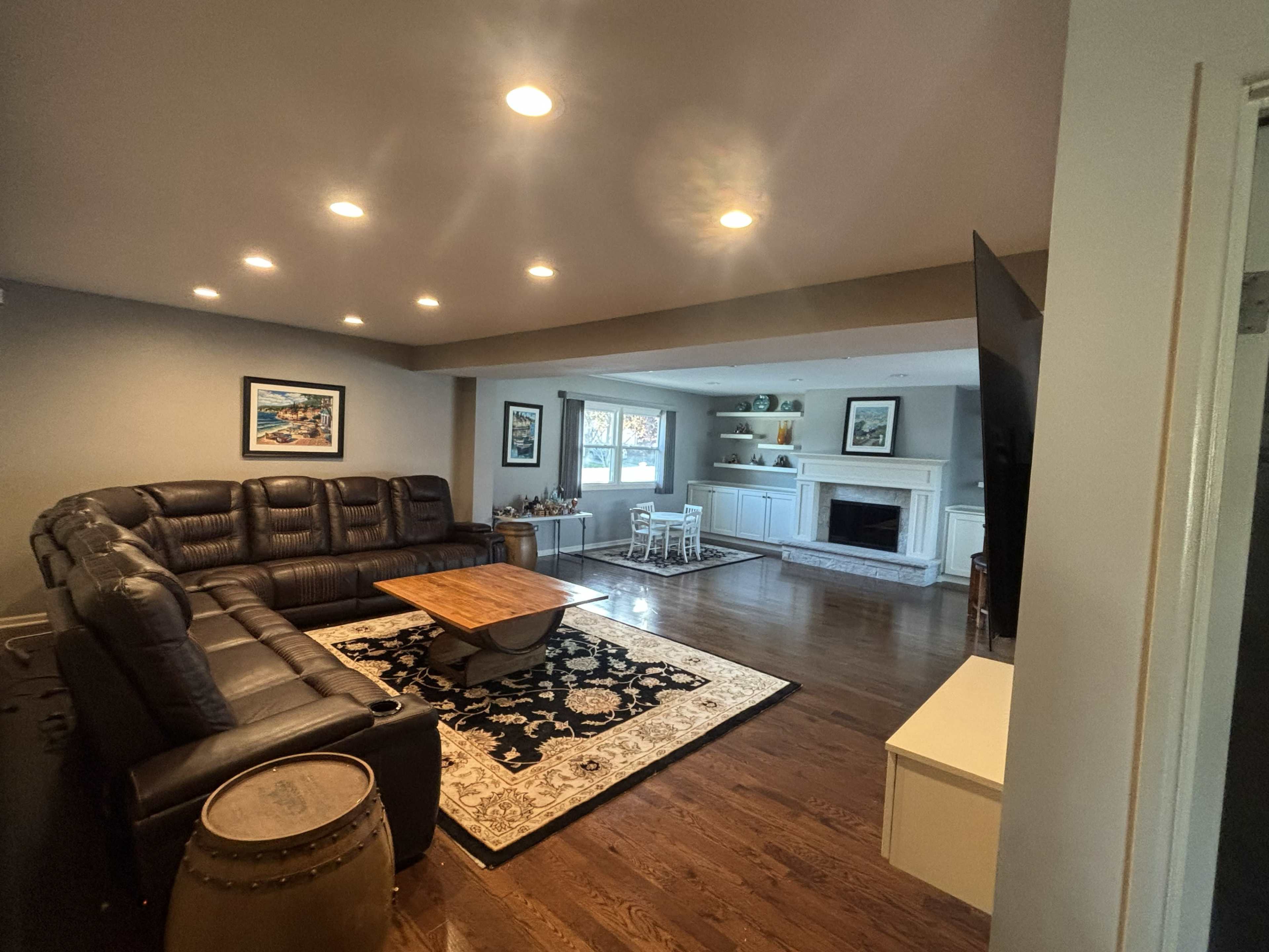 A spacious living room features a dark sectional sofa, a wooden coffee table, a patterned rug, and a white fireplace.