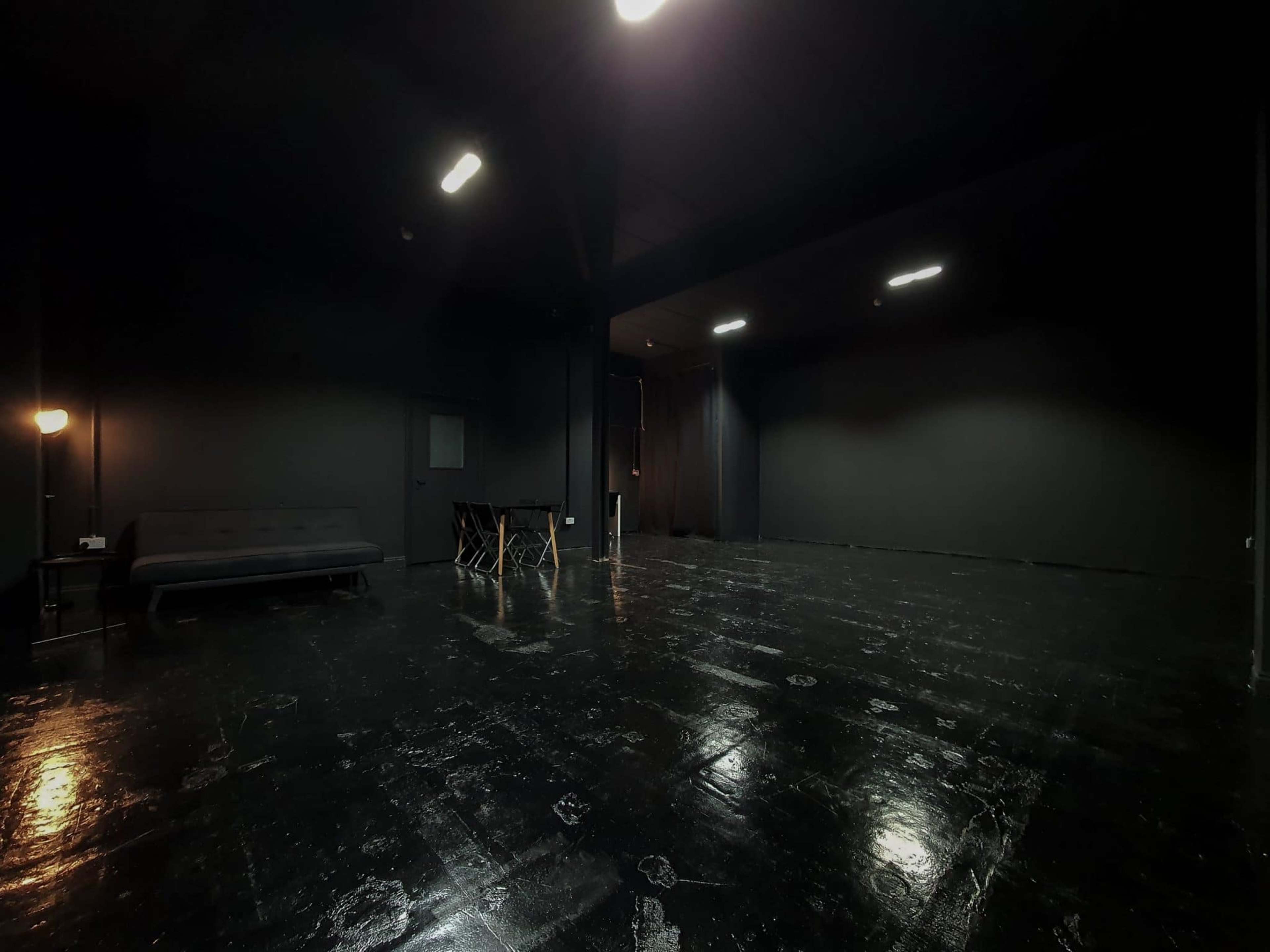 A dimly lit black room with a couch, a small table, and a sectioned area with dark walls.