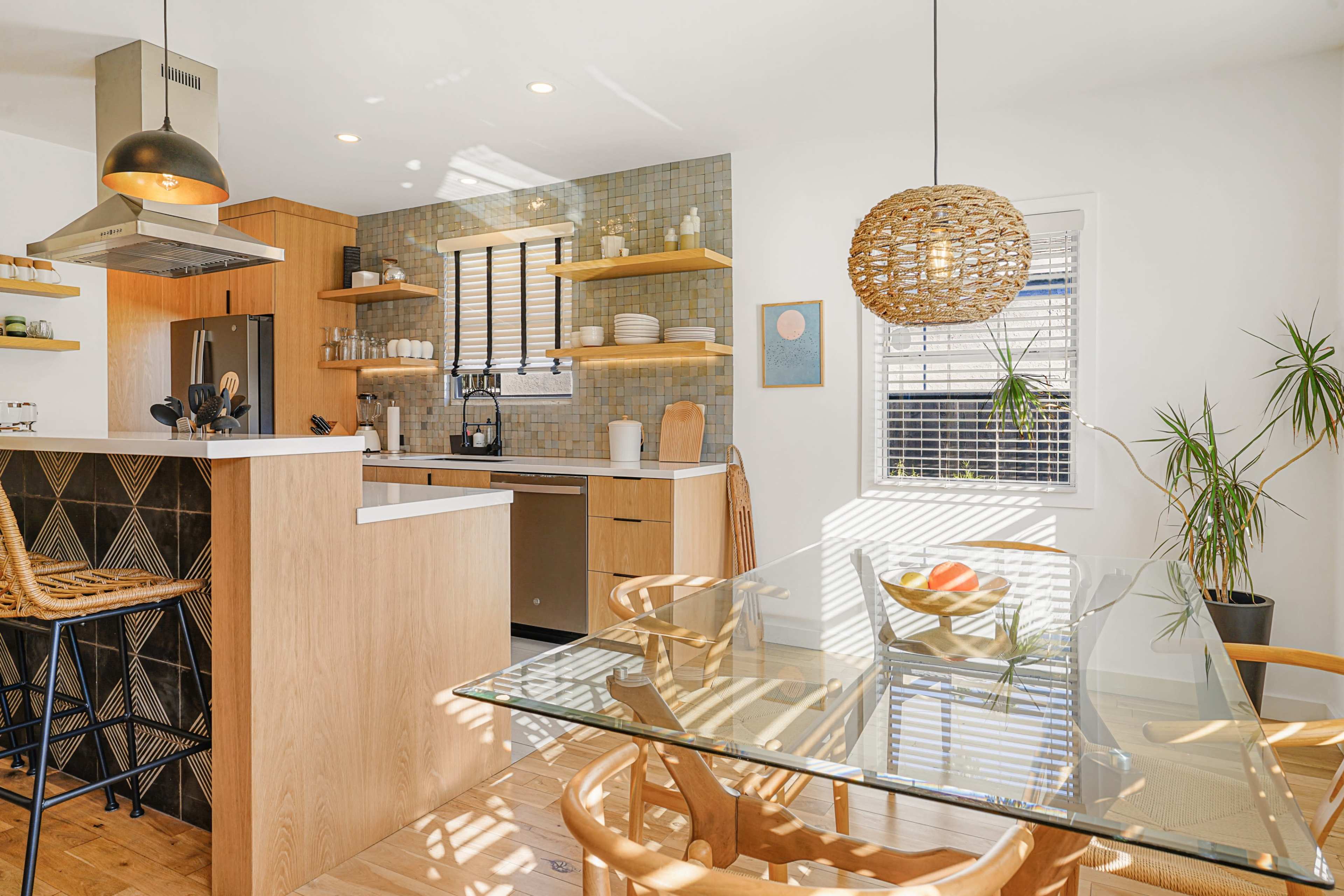 A modern kitchen and dining area featuring wooden cabinetry, a glass dining table, and a bright, open layout with natural light.
