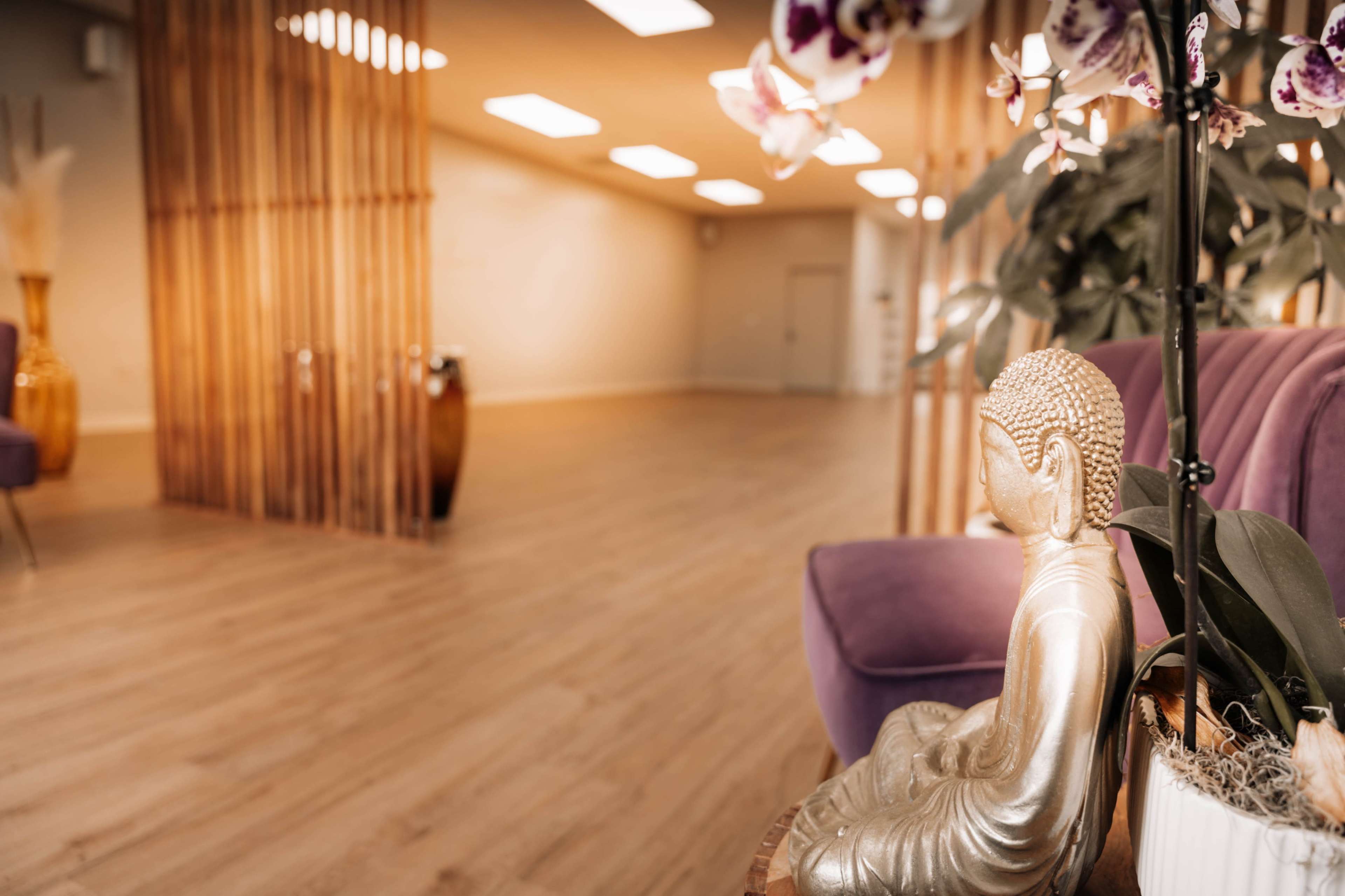 A serene interior space featuring a Buddha statue, a purple chair, and bamboo-like partitions, with plants and soft lighting.