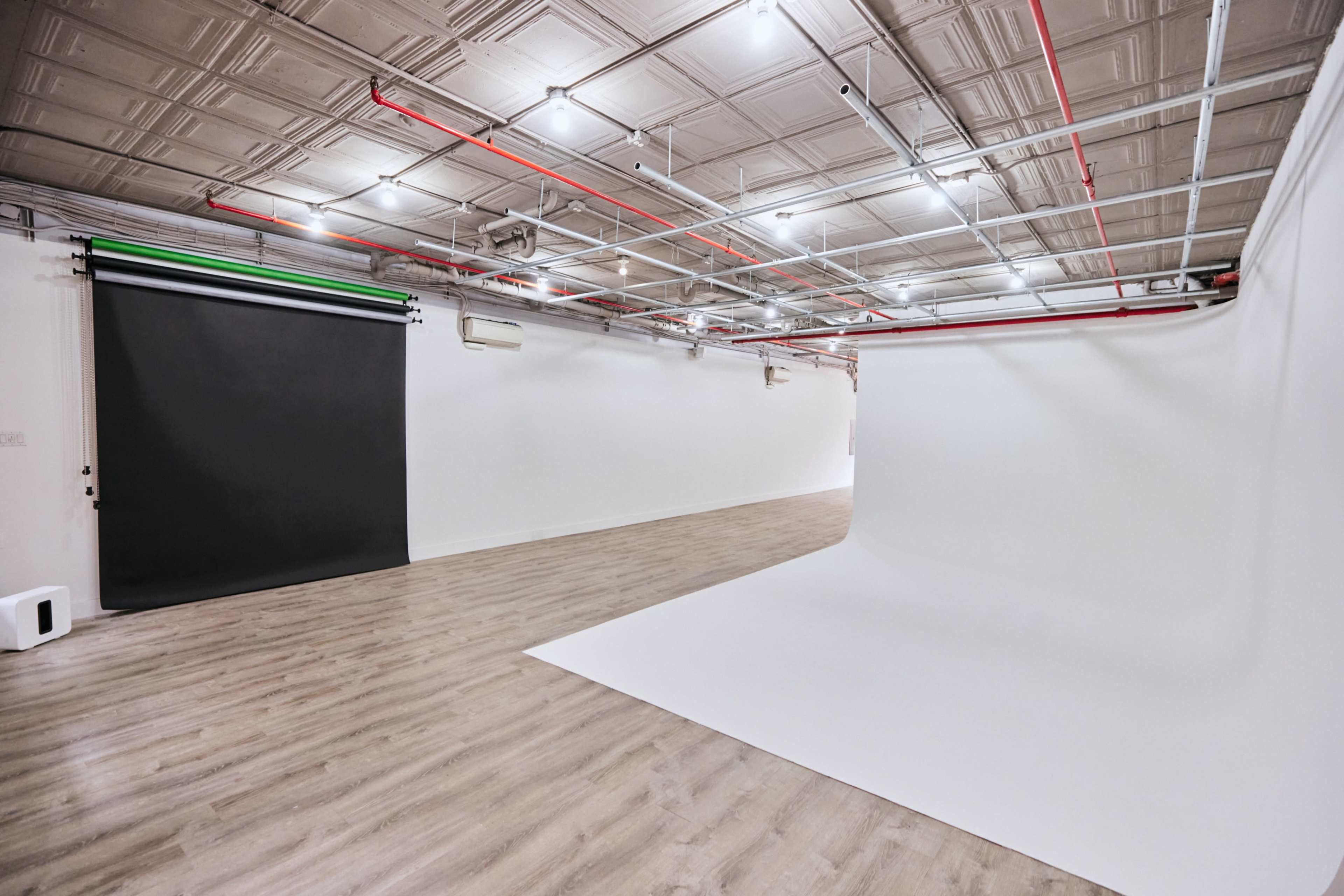 A spacious photography studio with two backdrop setups, one black and one white, and wooden flooring.