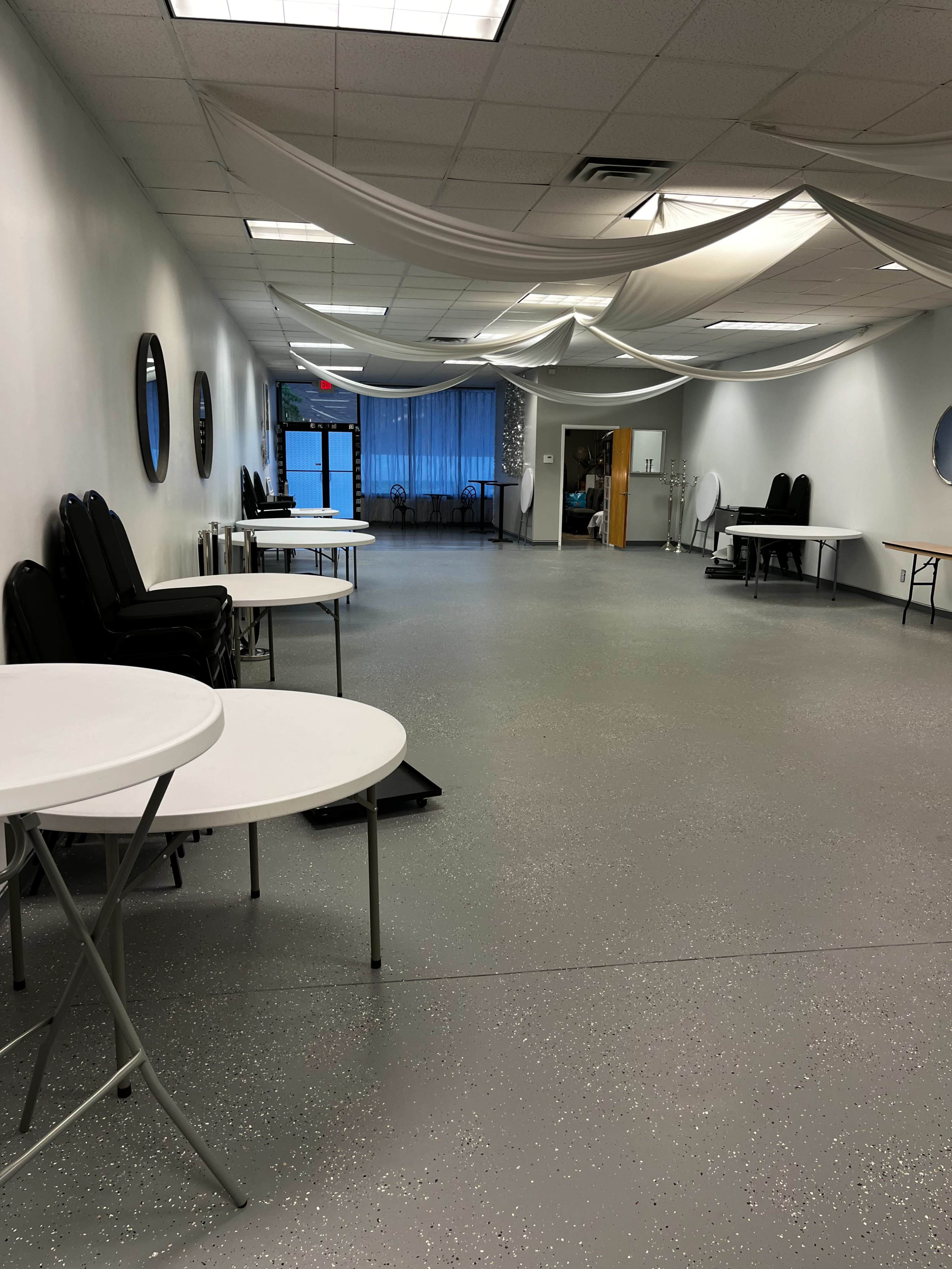 A spacious, empty room with white walls, folding tables, and draped fabric overhead.