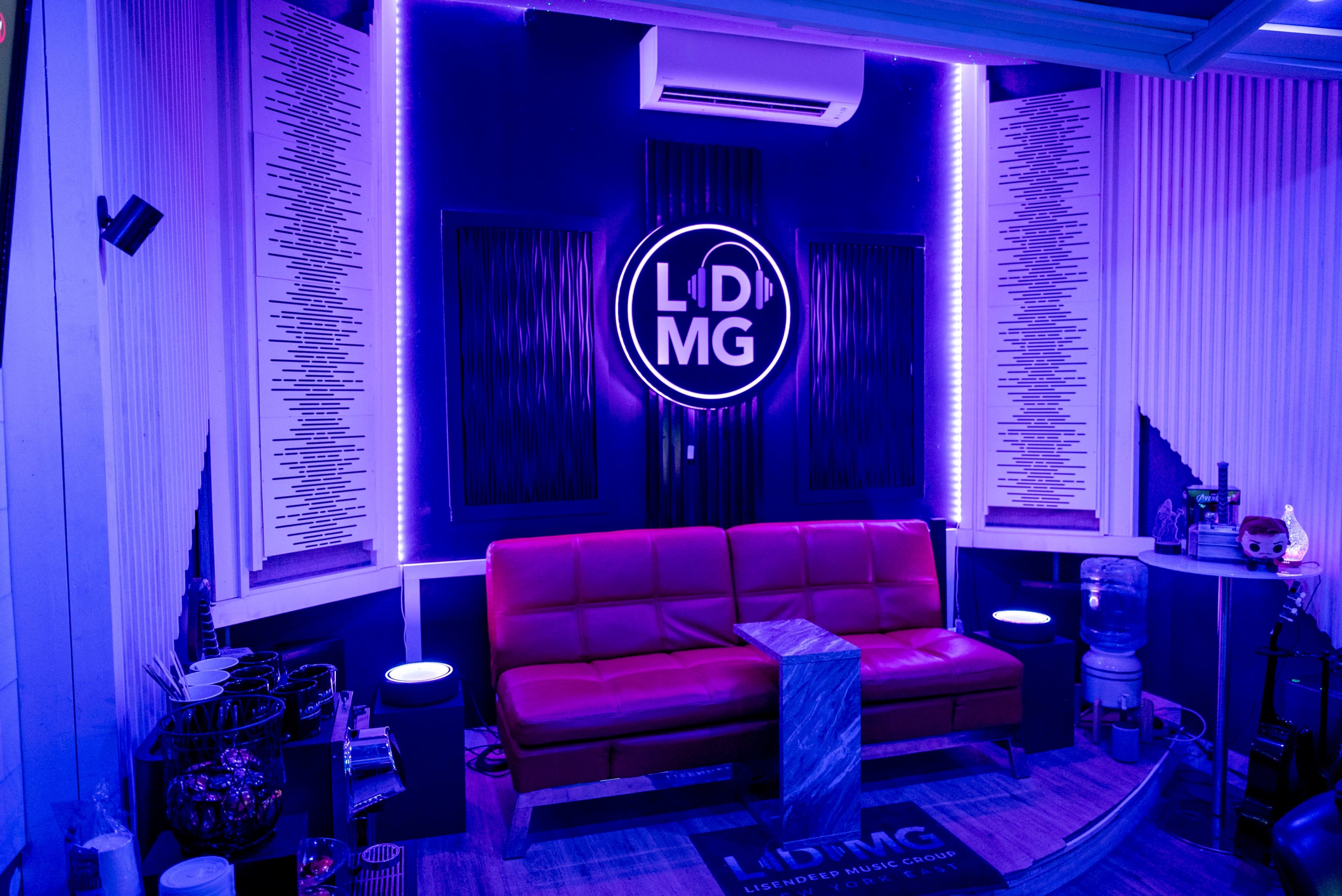 The image shows a modern lounge area with a red couch, illuminated by purple LED lights, and featuring a circular logo on the wall.