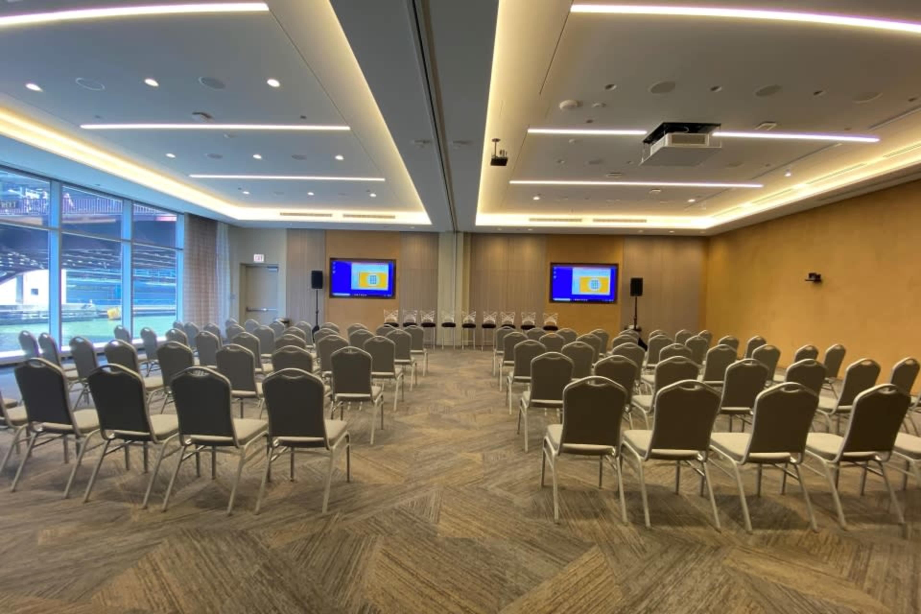 A conference room set up with rows of chairs facing two screens at the front.
