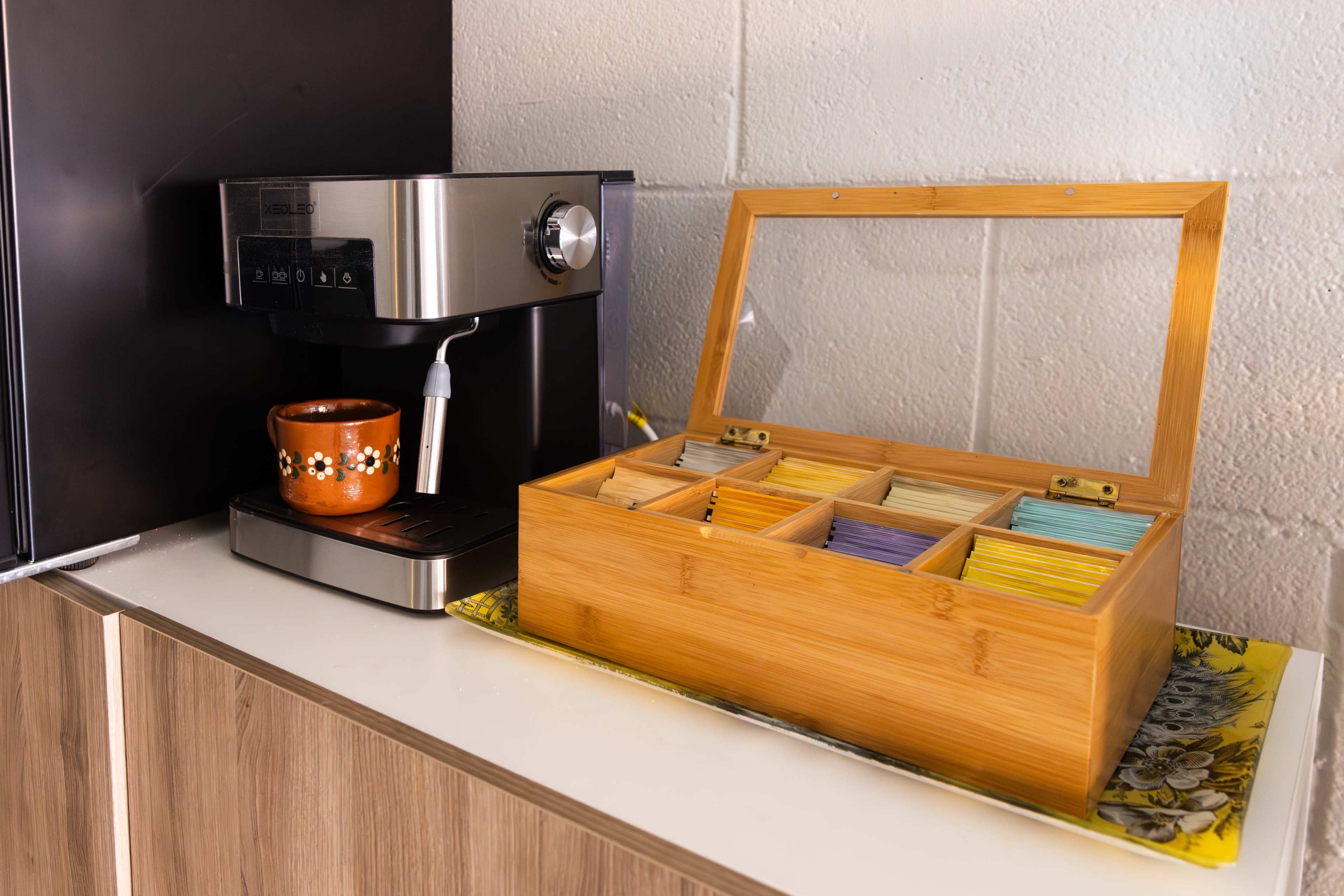 A coffee machine sits next to a wooden box containing assorted tea bags on a countertop.