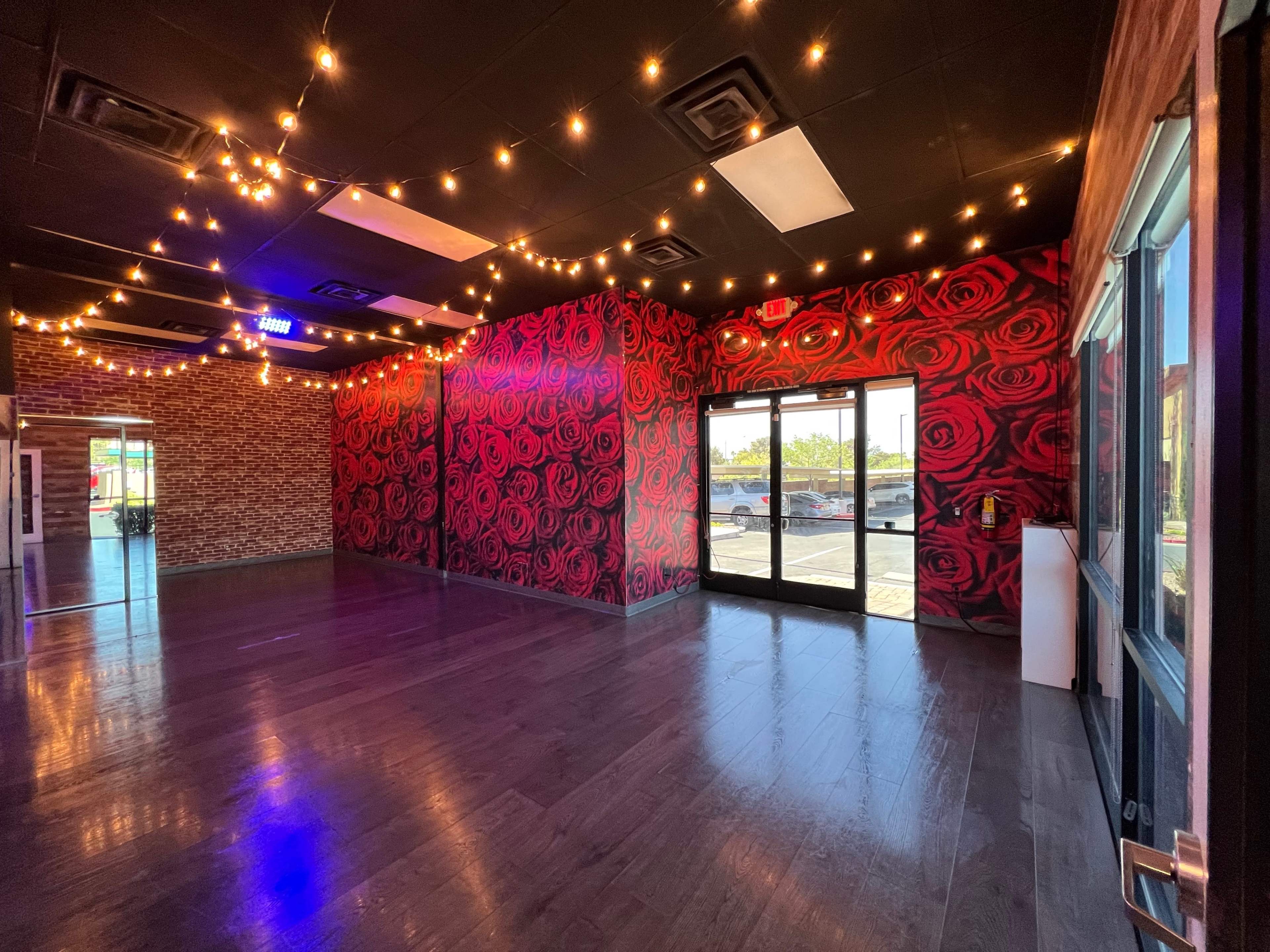 An empty room with dark wood floors, a wall decorated with red rose patterns, and string lights overhead.