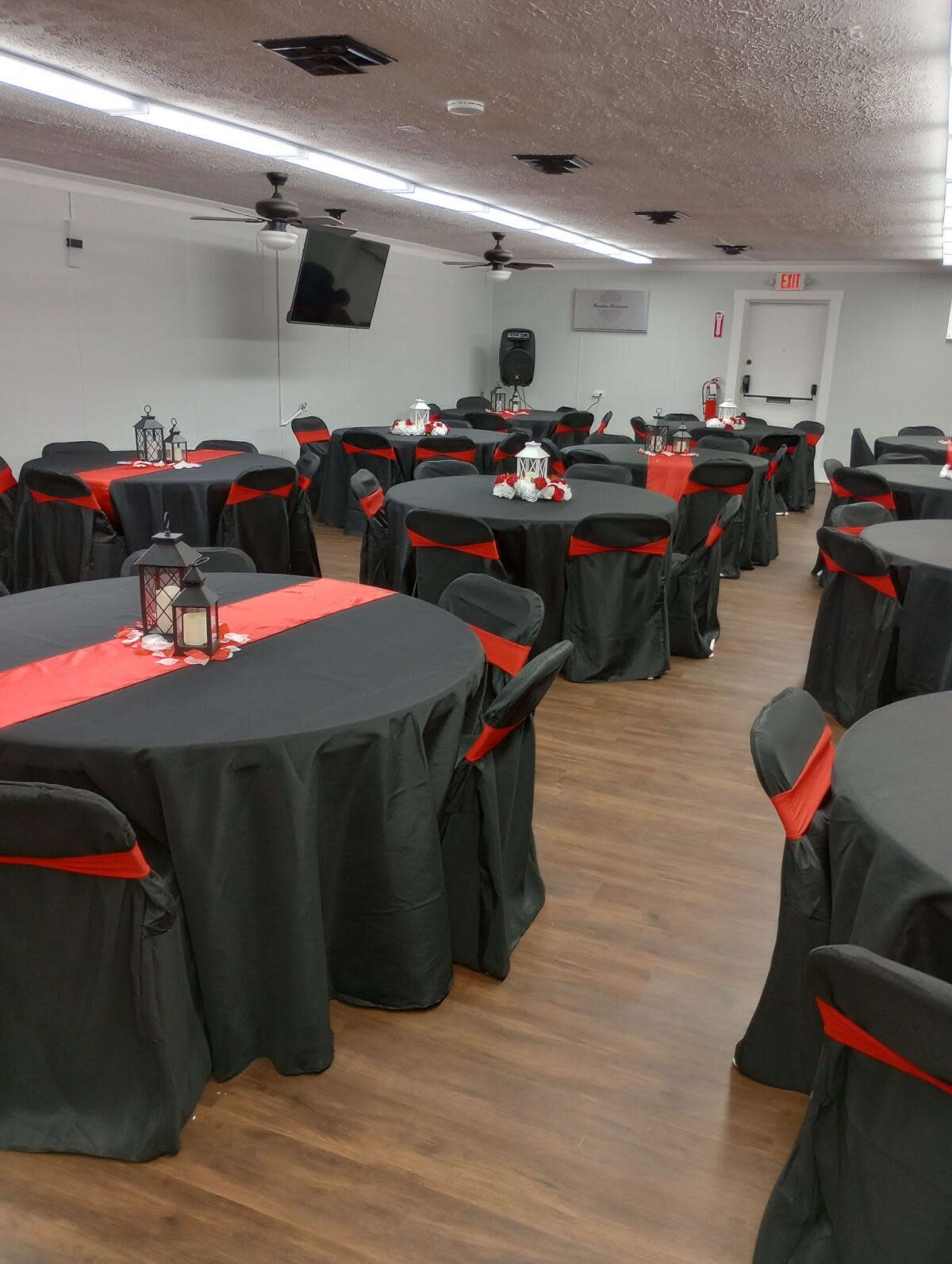 A banquet room arranged with round tables covered in black tablecloths accented by red runners, with chairs also draped in black fabric.