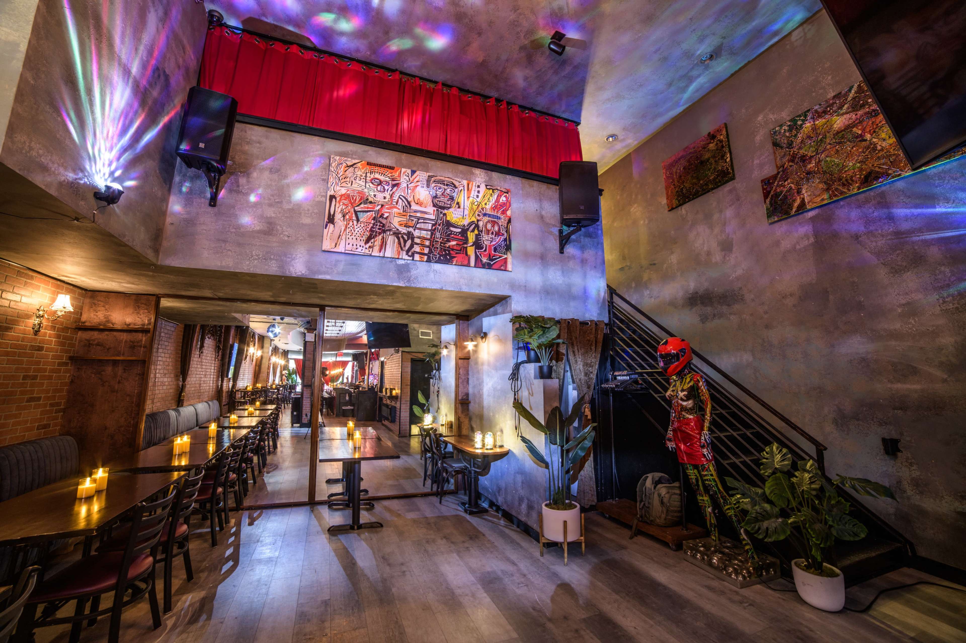 The image depicts a trendy restaurant interior featuring a staircase, a mirrored wall, and vibrant artwork illuminated by colorful lights.