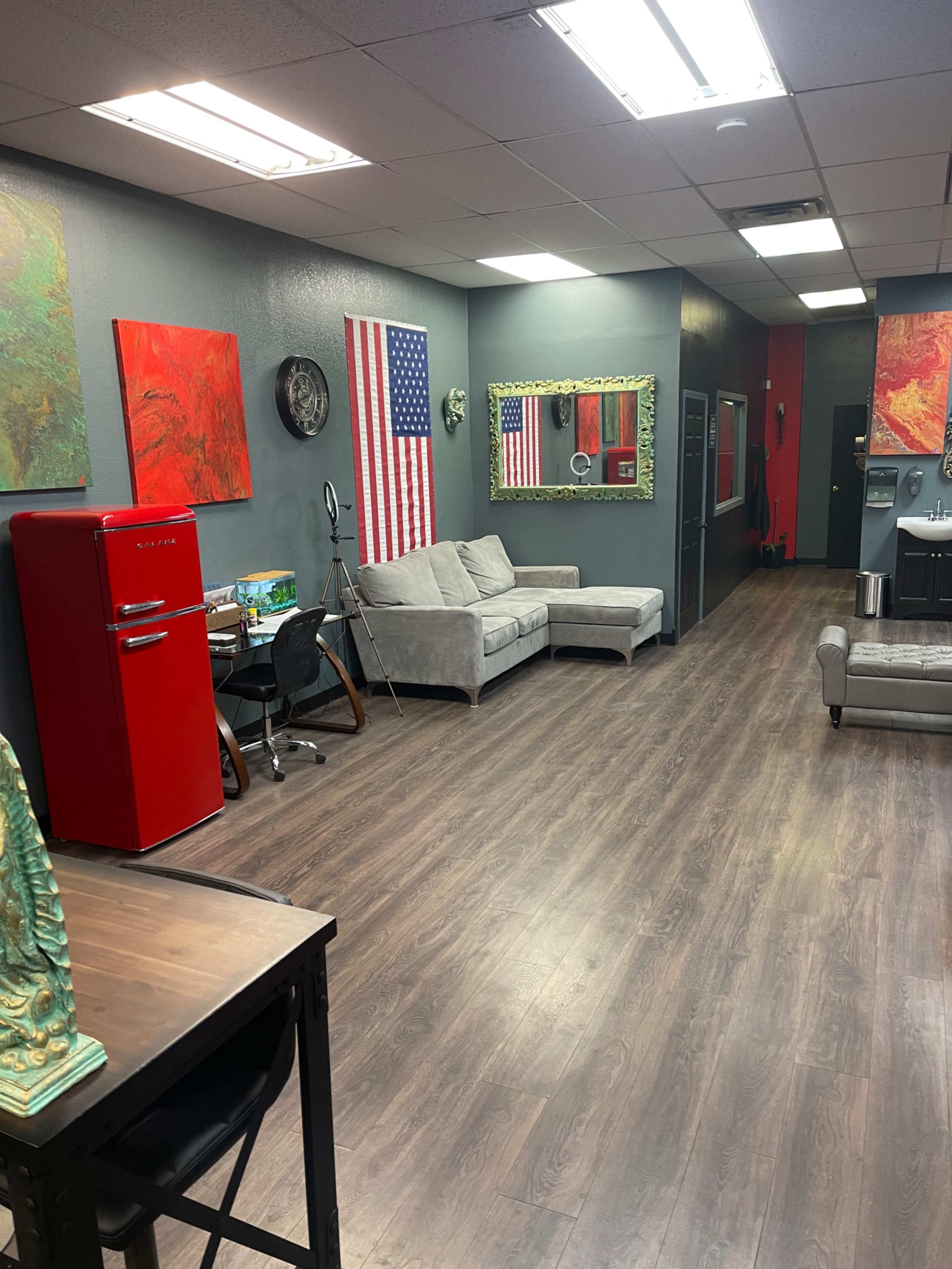 A spacious indoor area featuring gray walls, a red retro refrigerator, a couch, several pieces of artwork, and mirrors, with wooden flooring throughout.