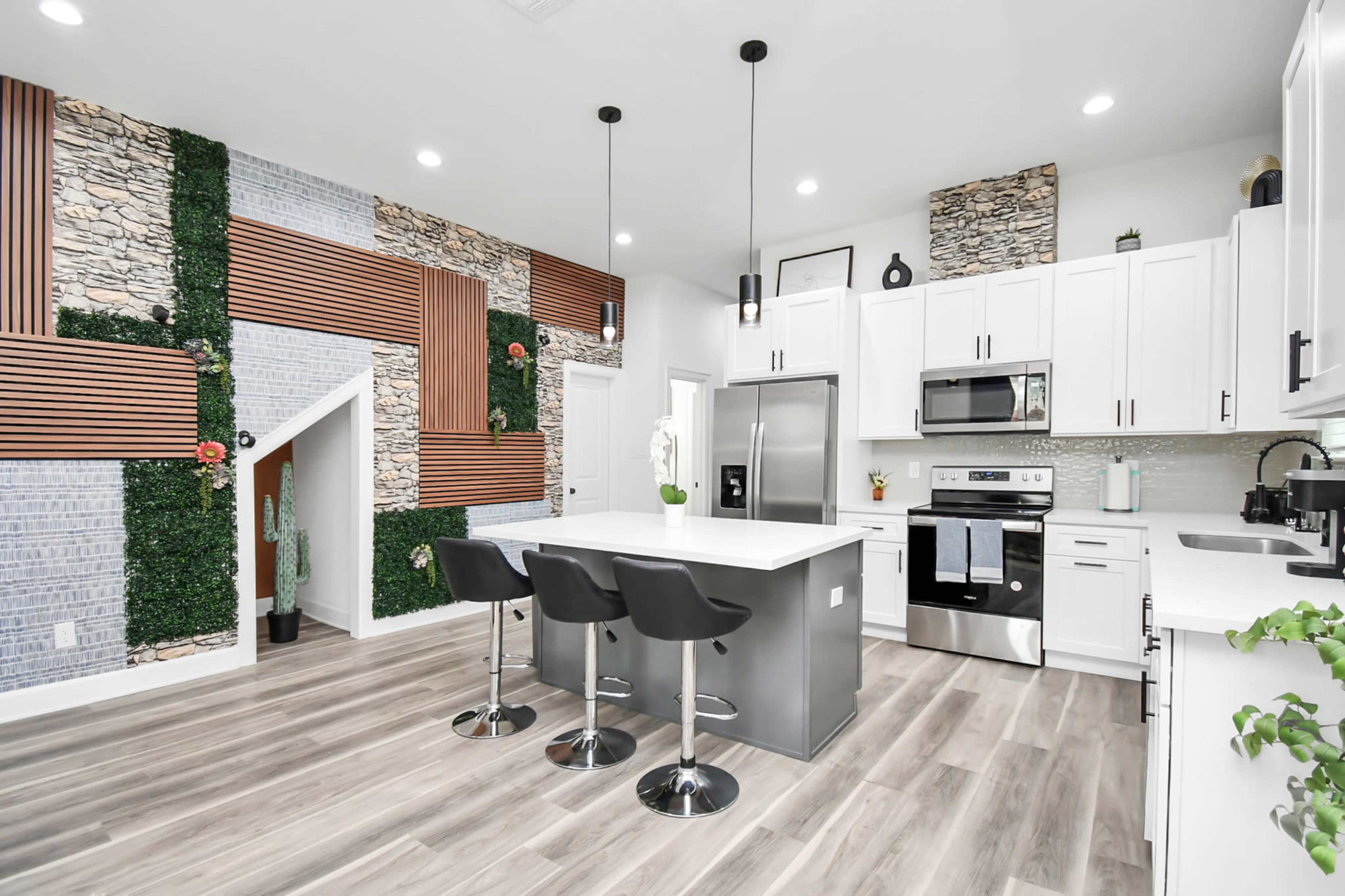 A modern kitchen featuring white cabinetry, stainless steel appliances, a central island with bar stools, and decorative wall elements including stone and wooden accents.