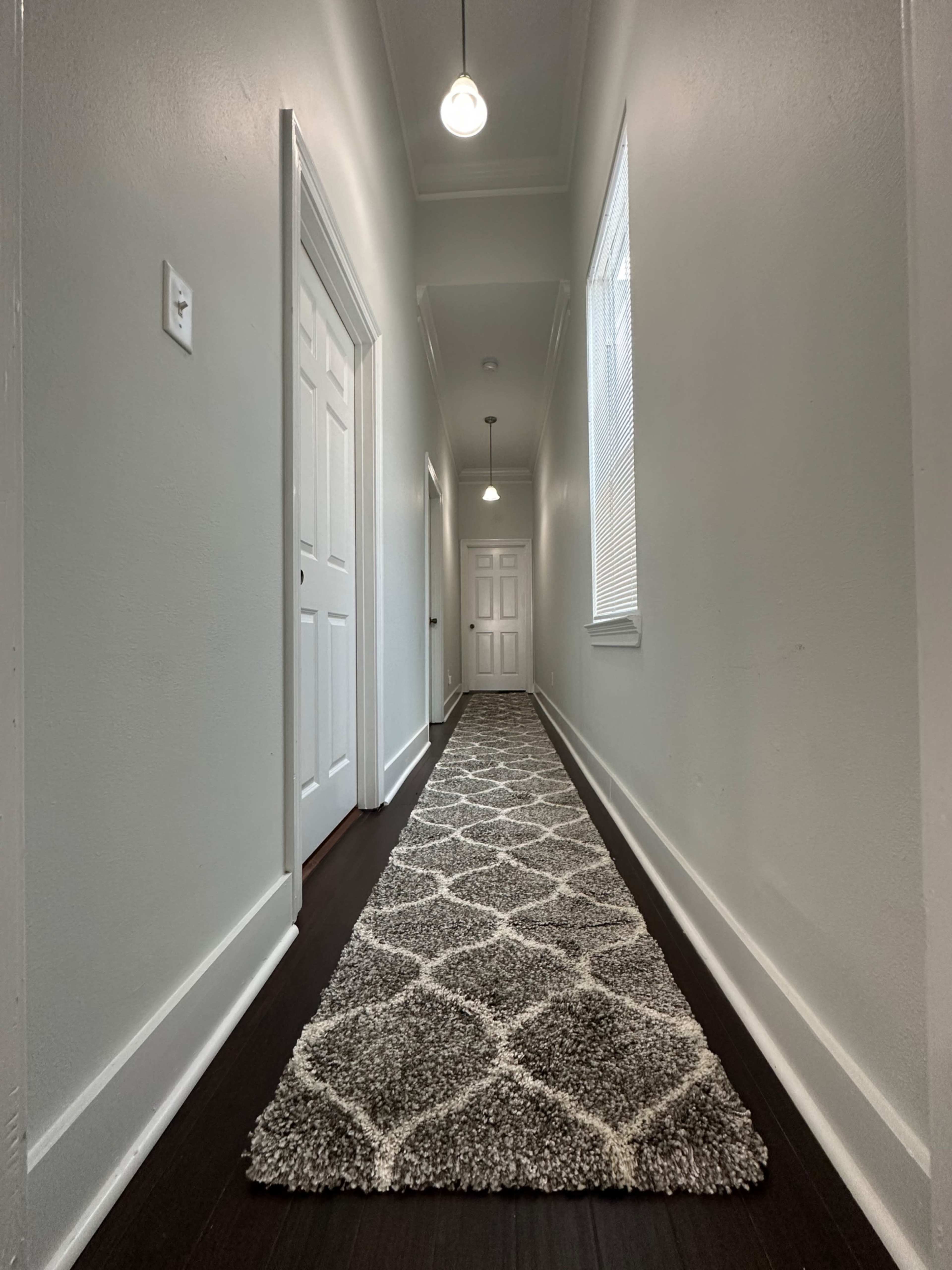 A long, narrow hallway with a patterned rug, white walls, and doors on either side.