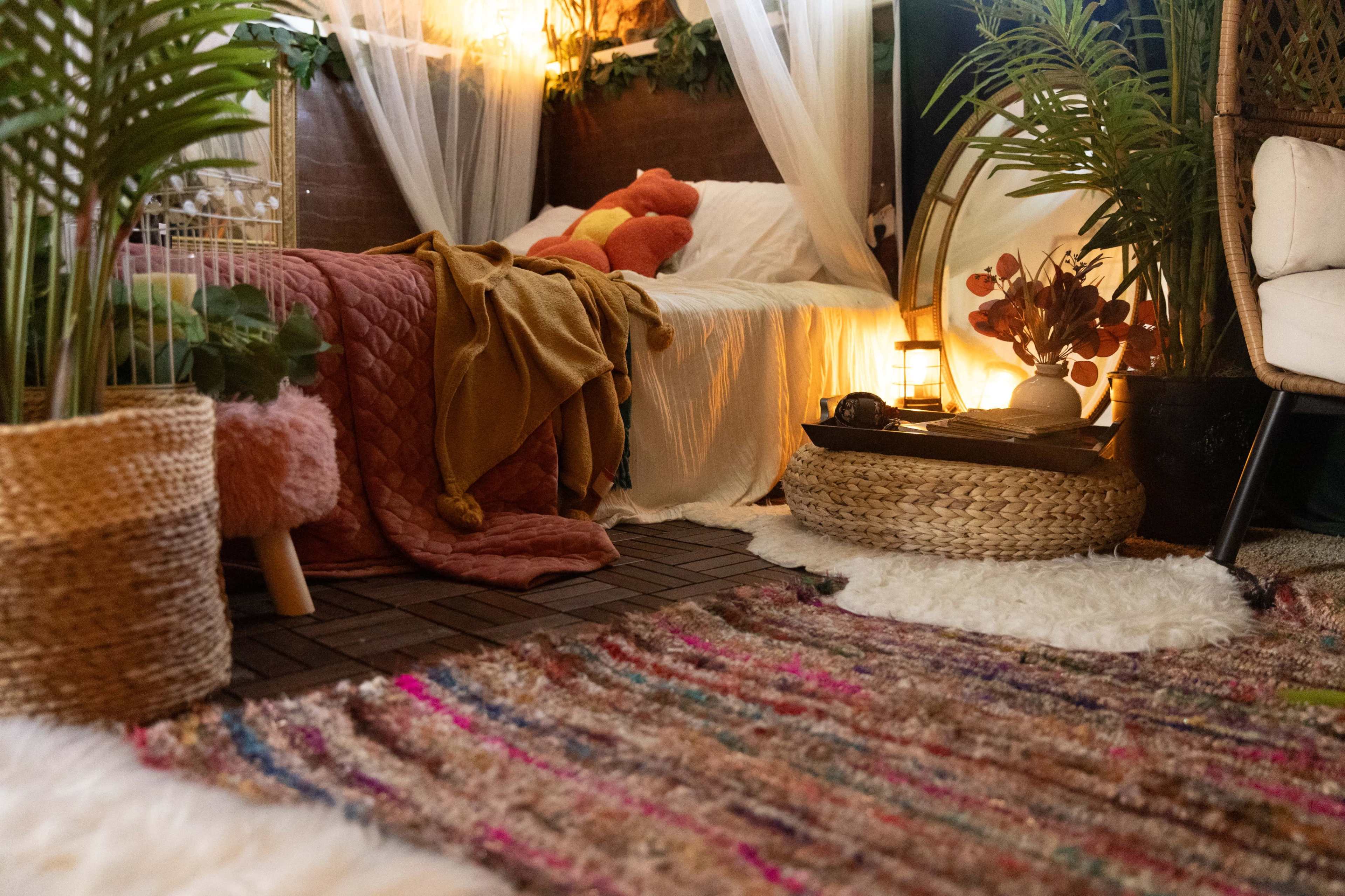 A cozy bedroom features a bed with soft blankets, a variety of plants, and a textured rug on the floor.