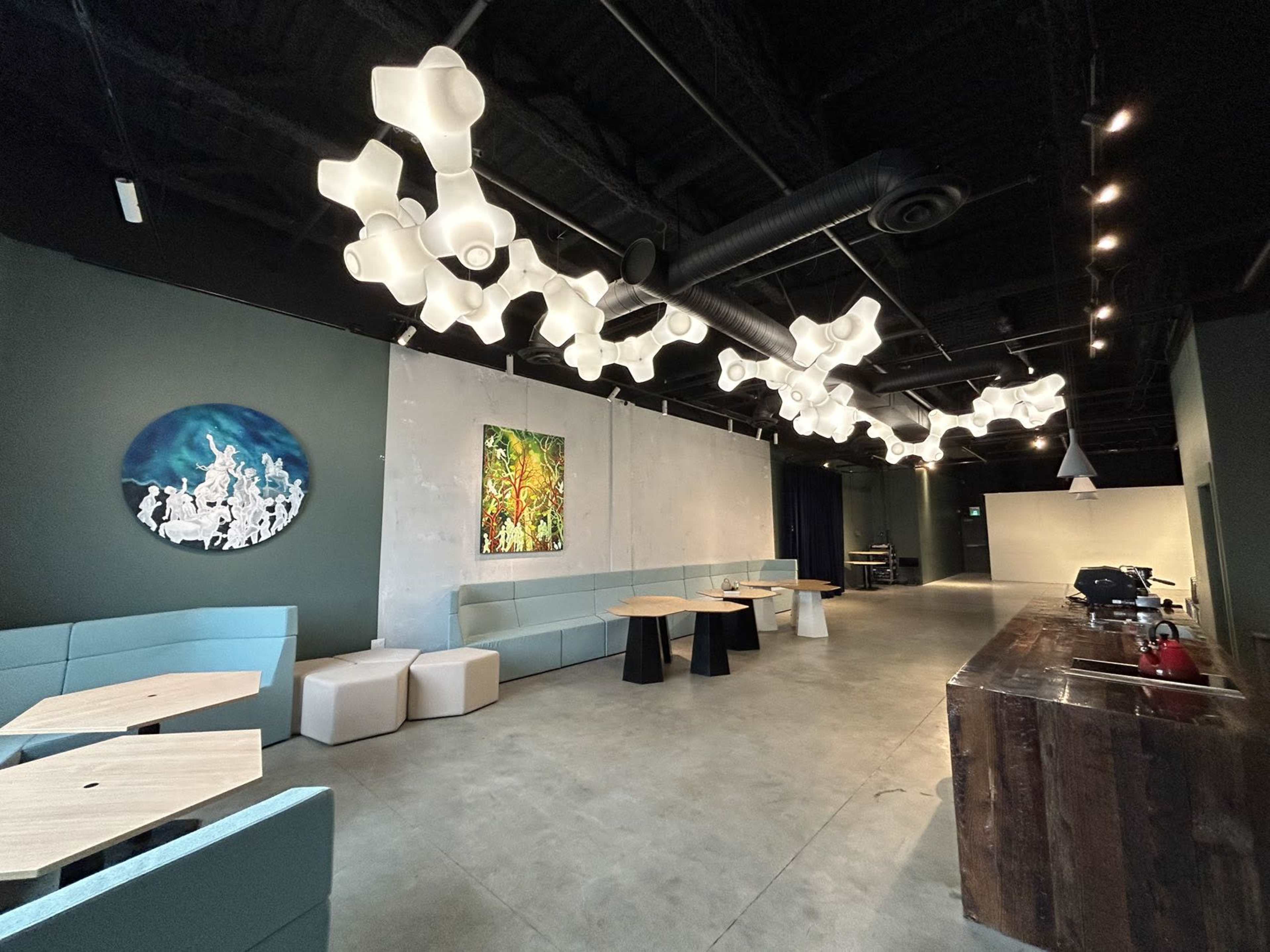 The image shows a modern interior of a café with unique lighting fixtures, various seating arrangements, and colorful artwork on the walls.