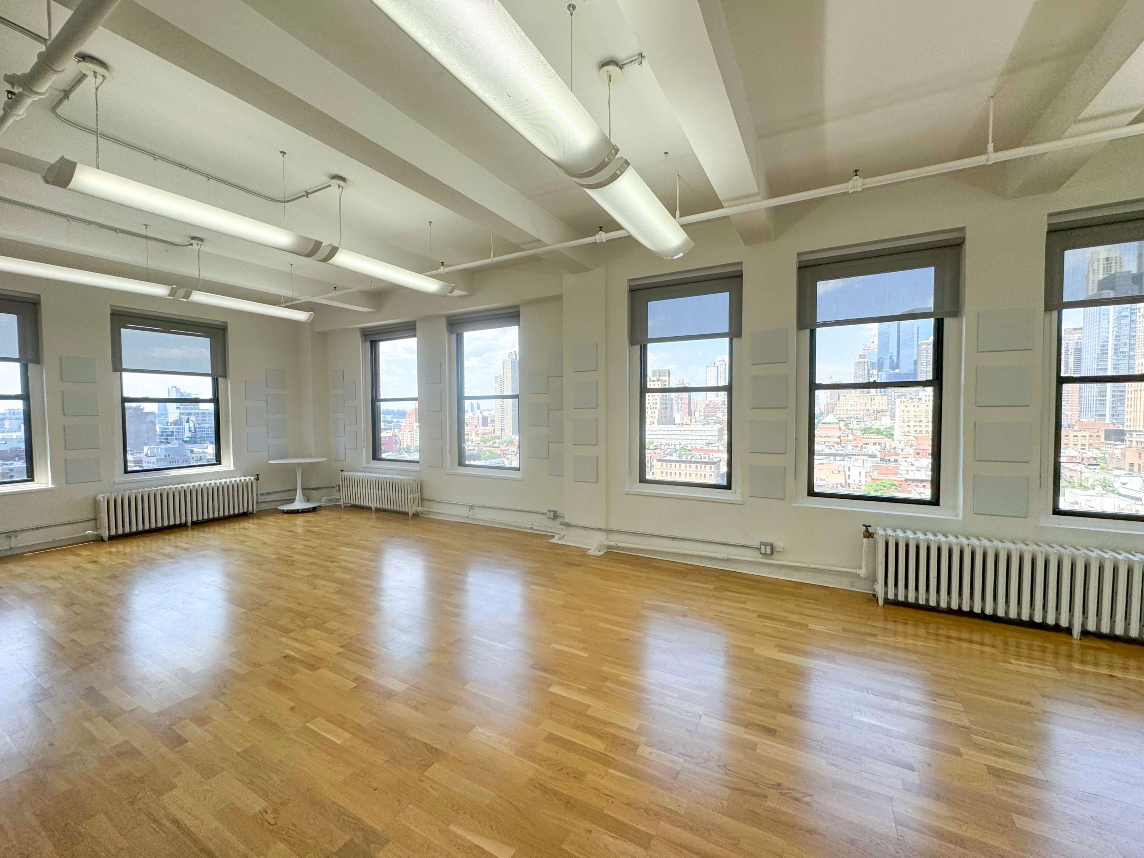A spacious, empty room with large windows overlooking a cityscape is illuminated by natural light.