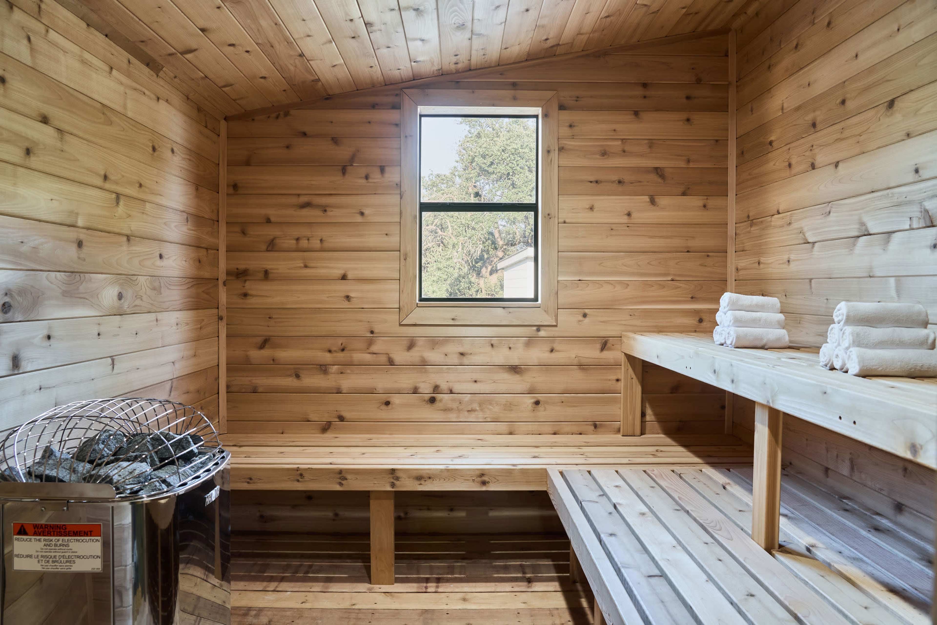 The image shows a wooden sauna with benches, a window, and neatly rolled towels placed on a shelf.