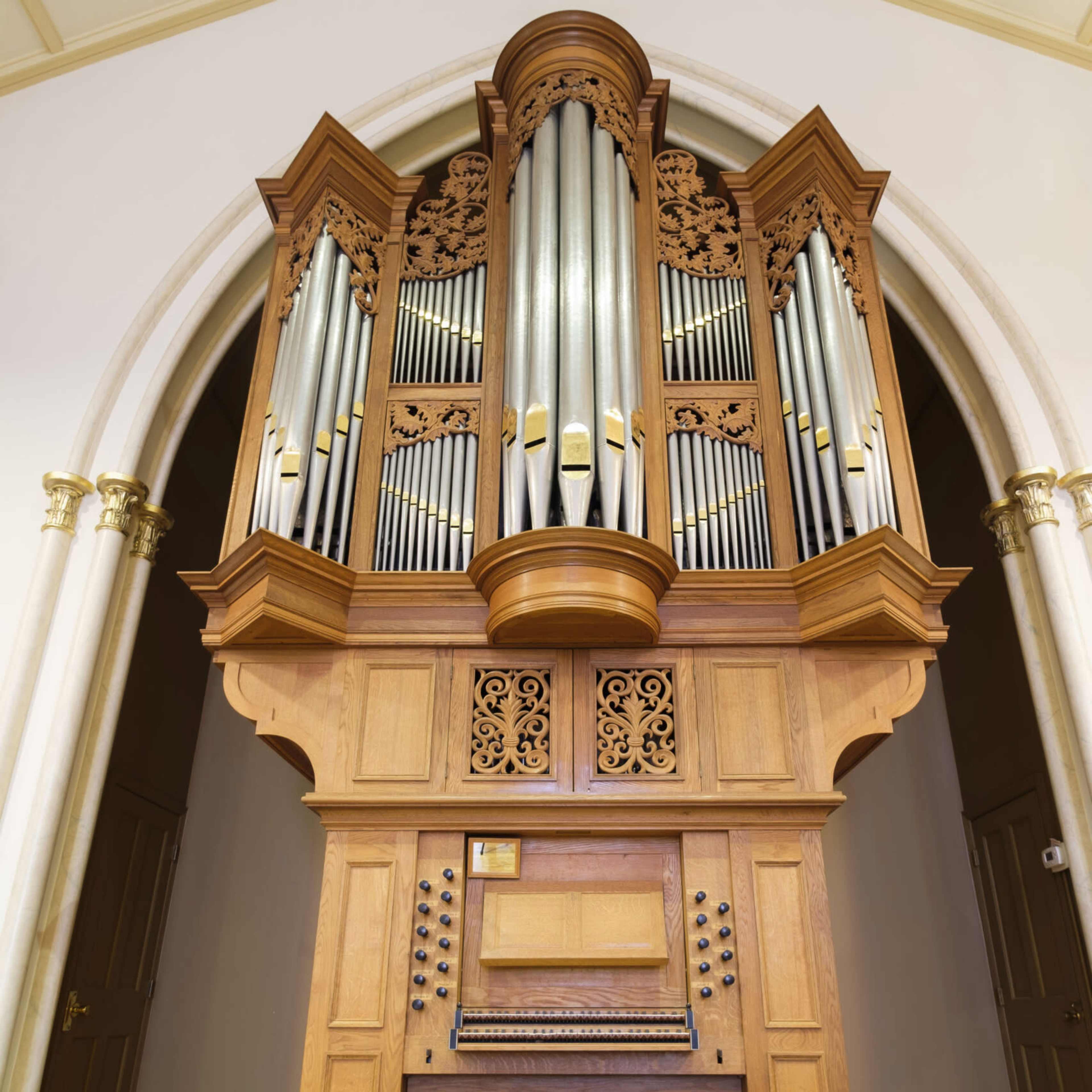 A wooden pipe organ with intricate carvings, featuring multiple silver pipes arranged in a decorative housing.