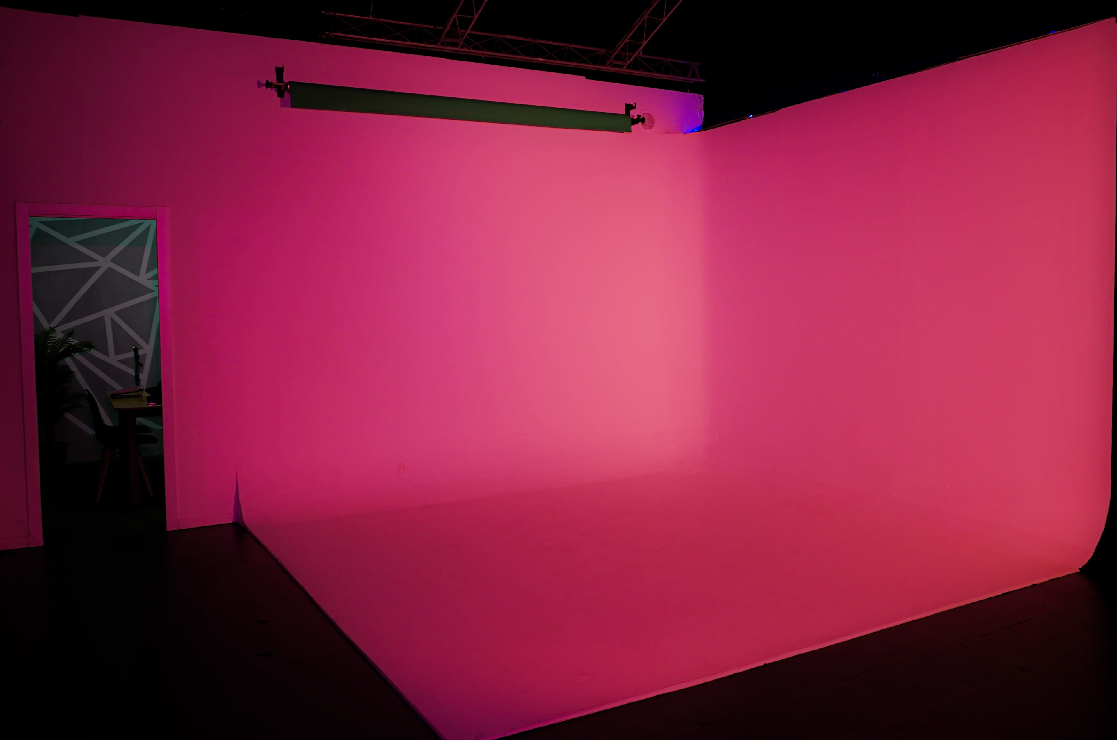A studio space features a pink-lit backdrop with a doorway visible on the left.