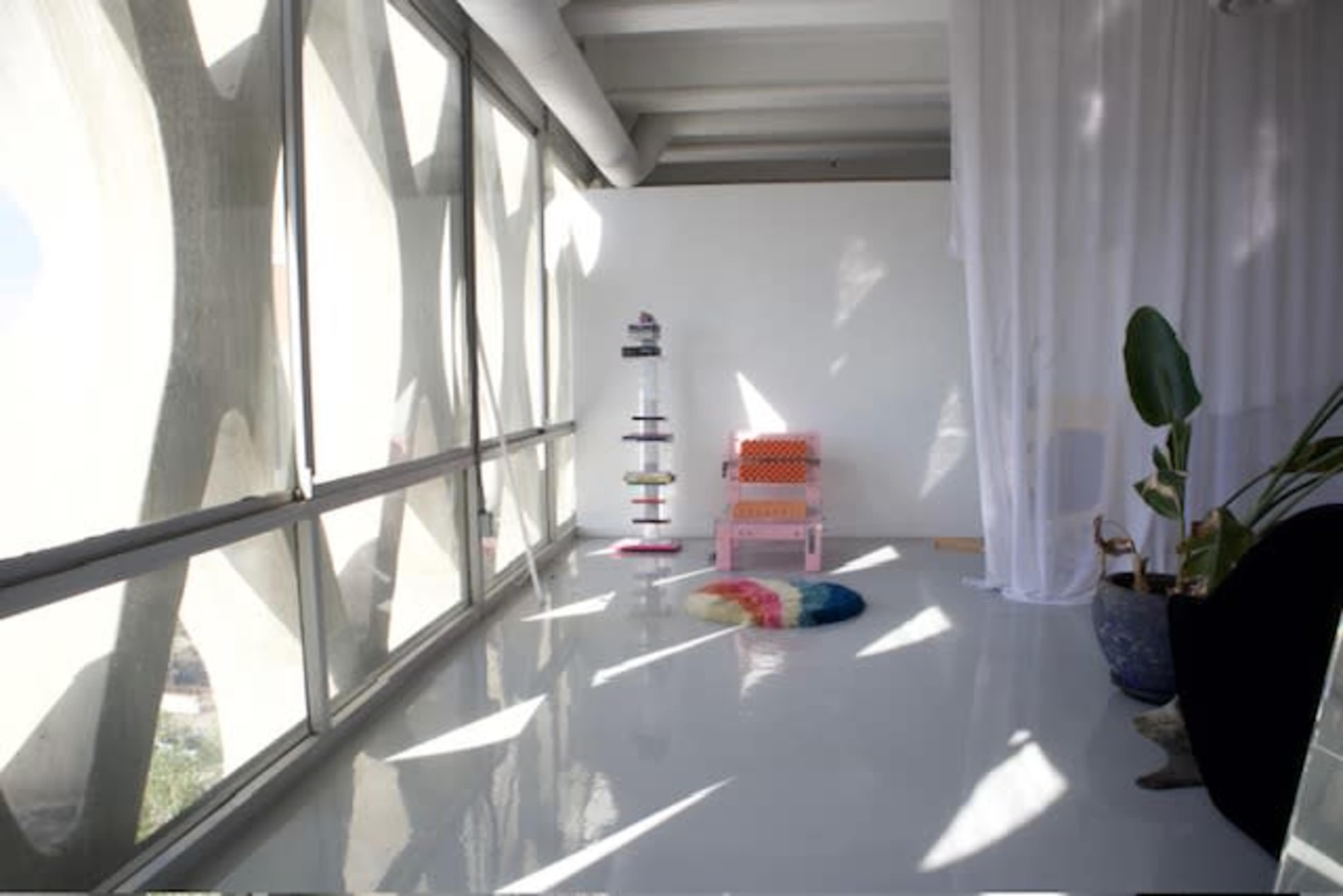 A bright indoor space with large windows, a colorful chair, a decorative plant, and a minimalist design.