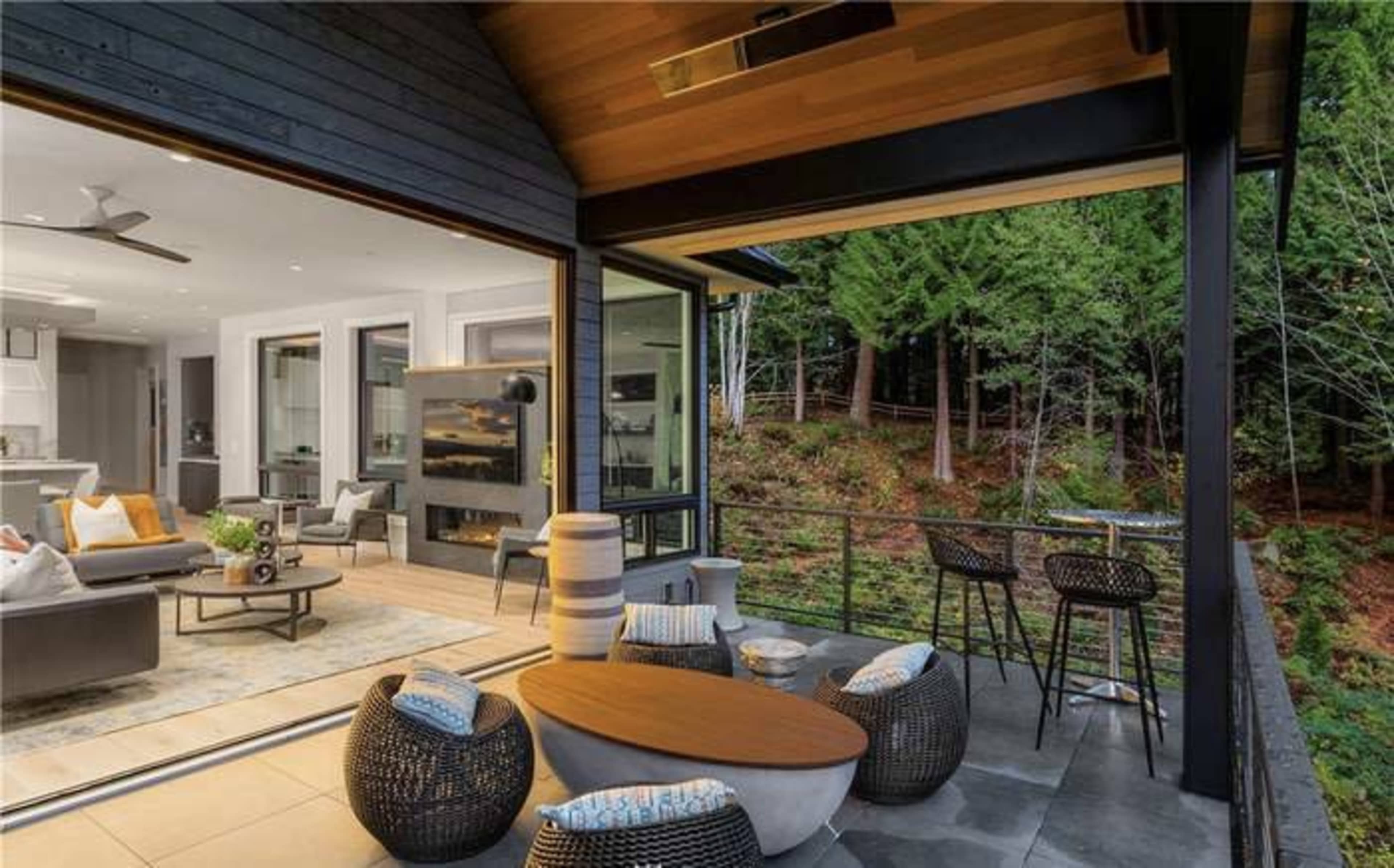 A modern outdoor patio area with comfortable seating, a small wooden table, and a view of a forested landscape.