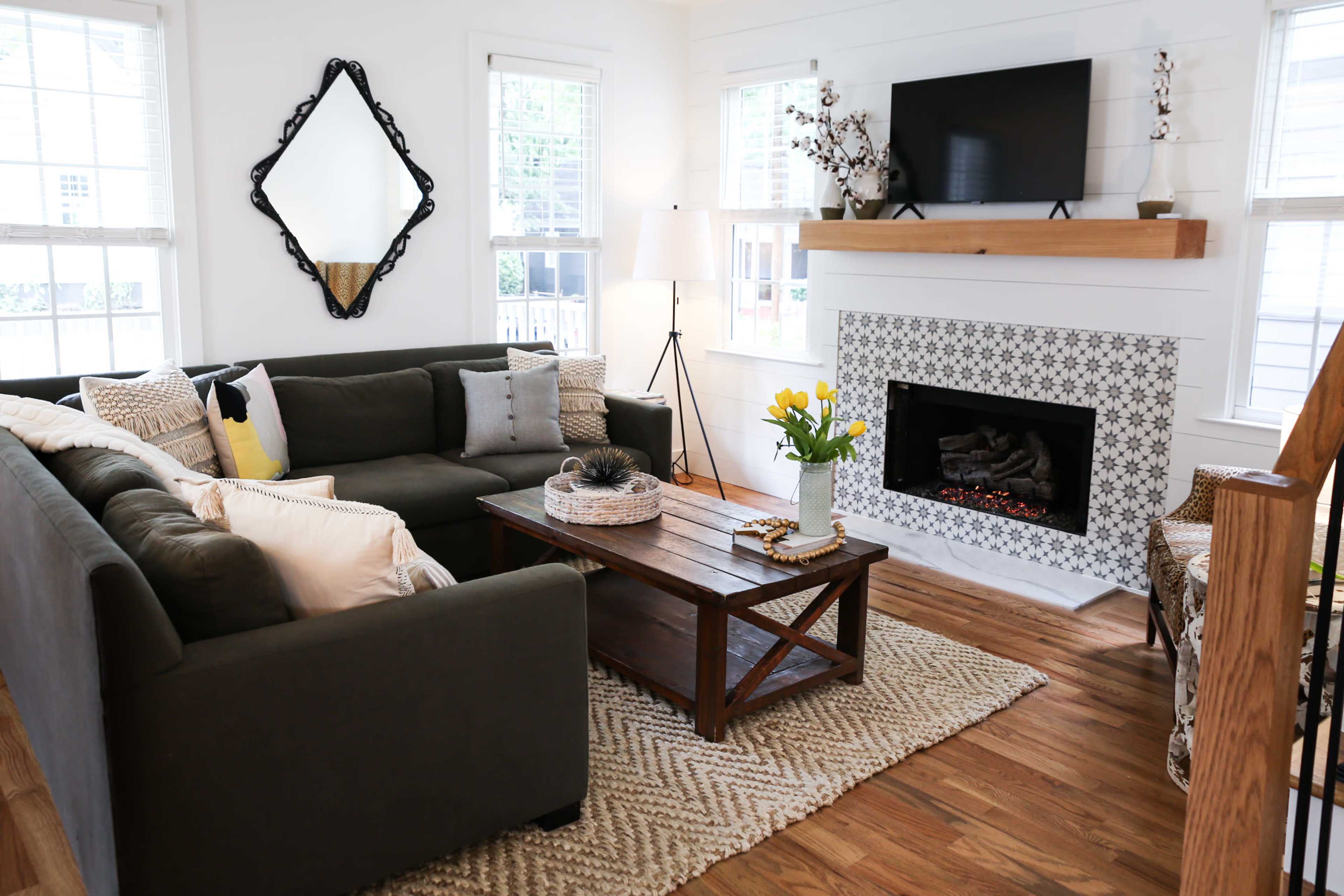 The living room features a sectional sofa, a wooden coffee table with decorative items, and a fireplace with a tiled surround, all arranged around a television mounted on the wall.
