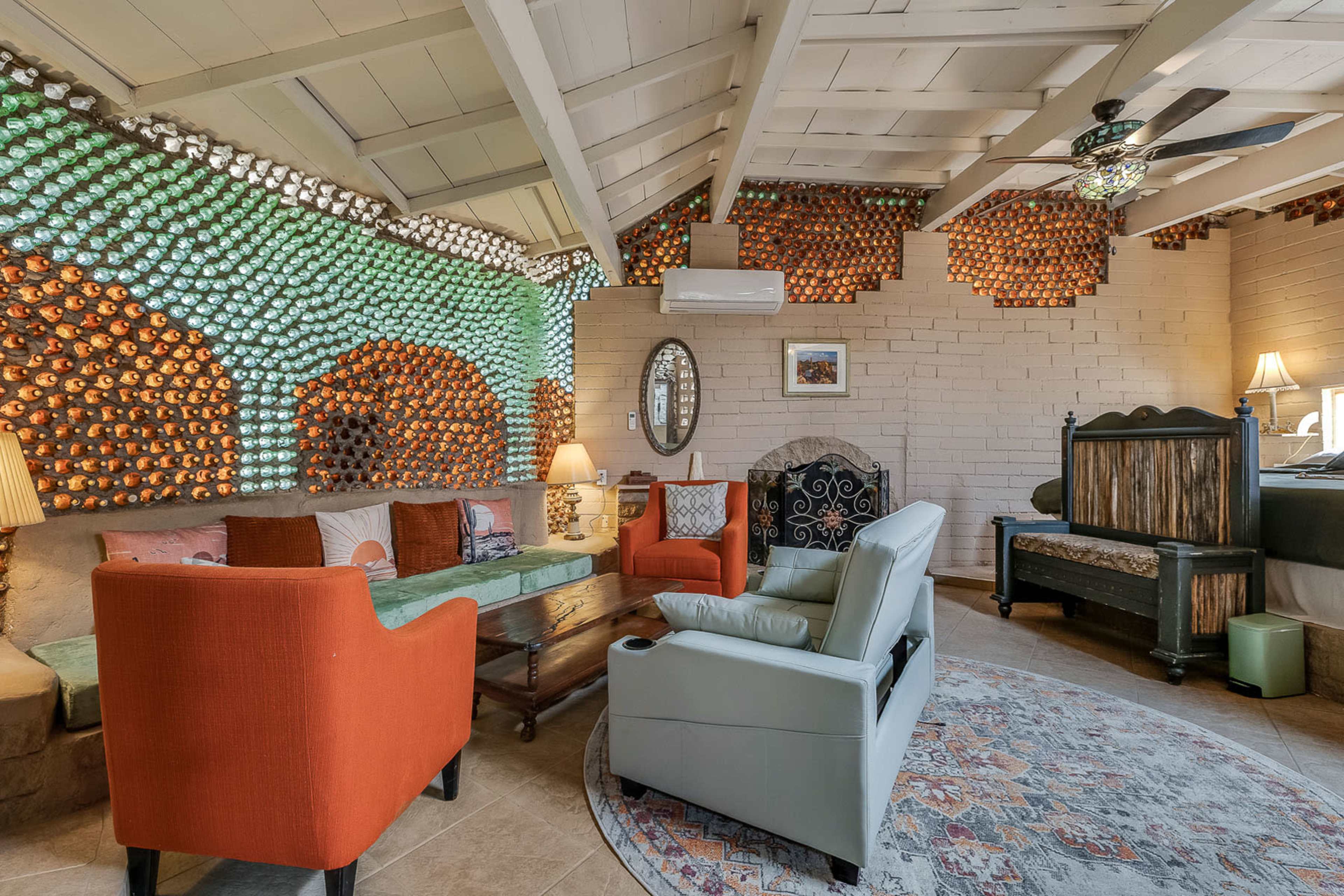 The scene shows a cozy living room with a unique wall made of colorful round objects, featuring a mix of seating options, including orange and light gray chairs, and wooden accents.