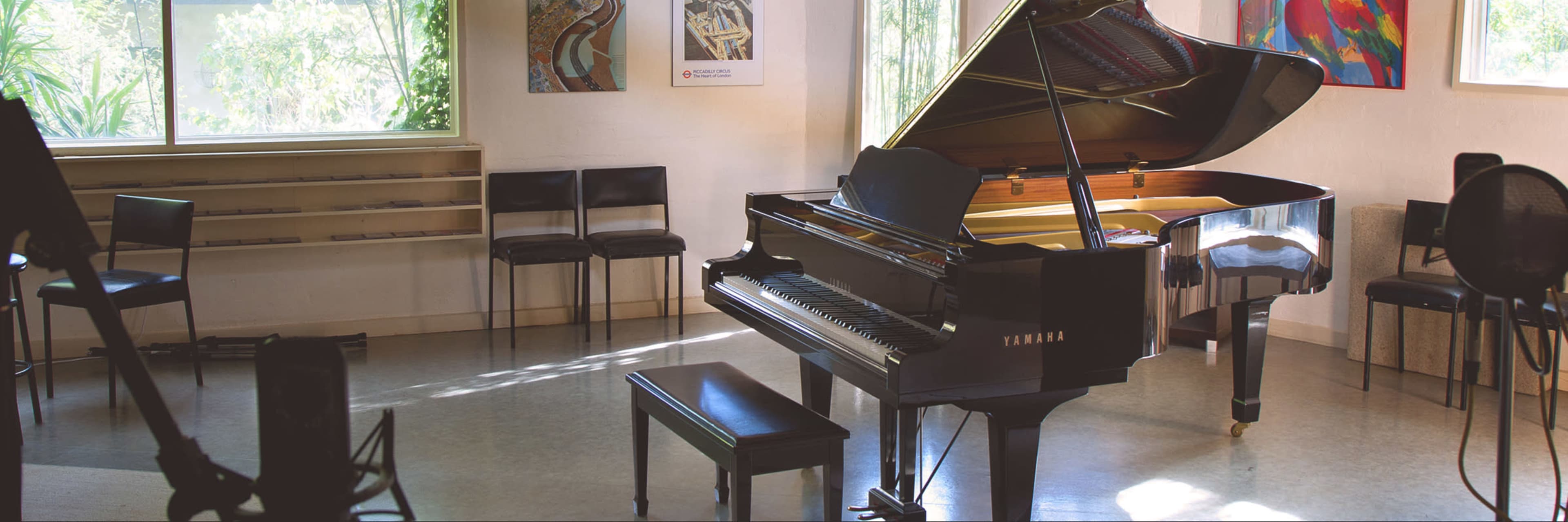 A grand piano is positioned in a well-lit music room with chairs and artwork on the walls.