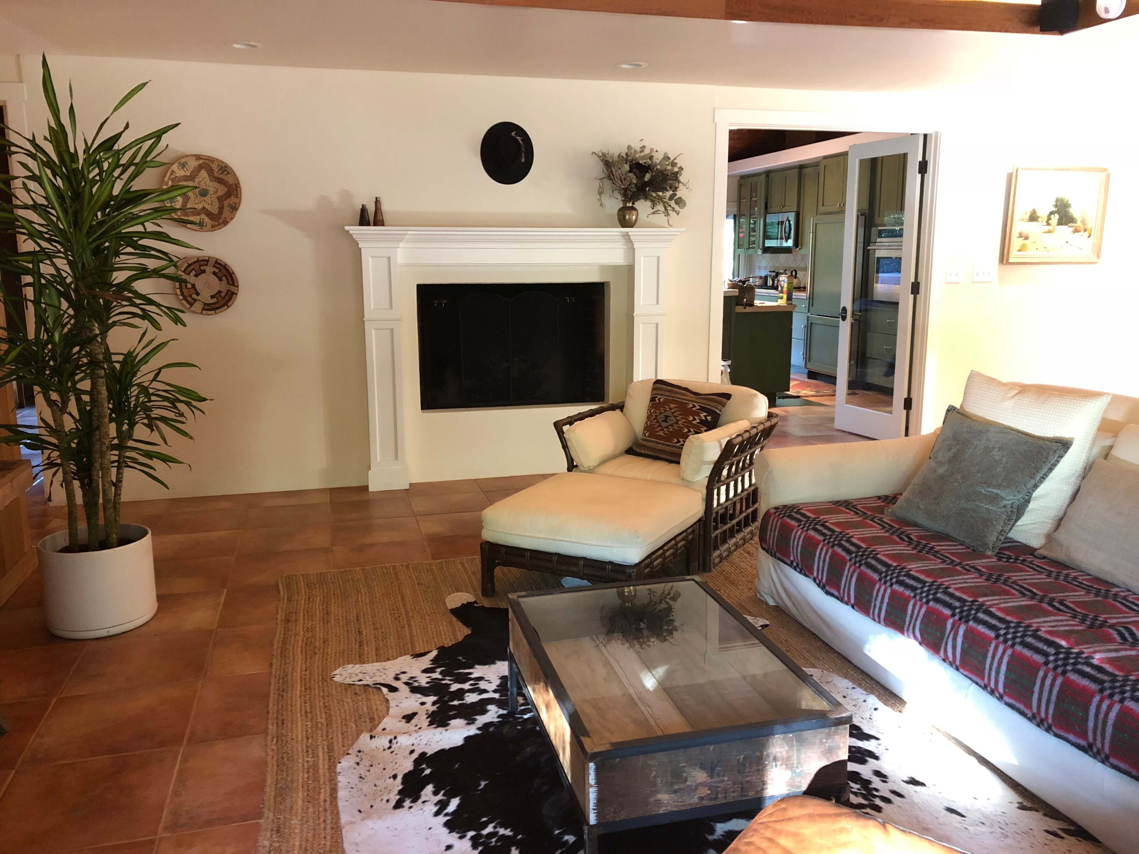 The living room features a mix of furniture, including a wicker chair, a couch with a plaid throw, a coffee table, and decorative items on the walls.