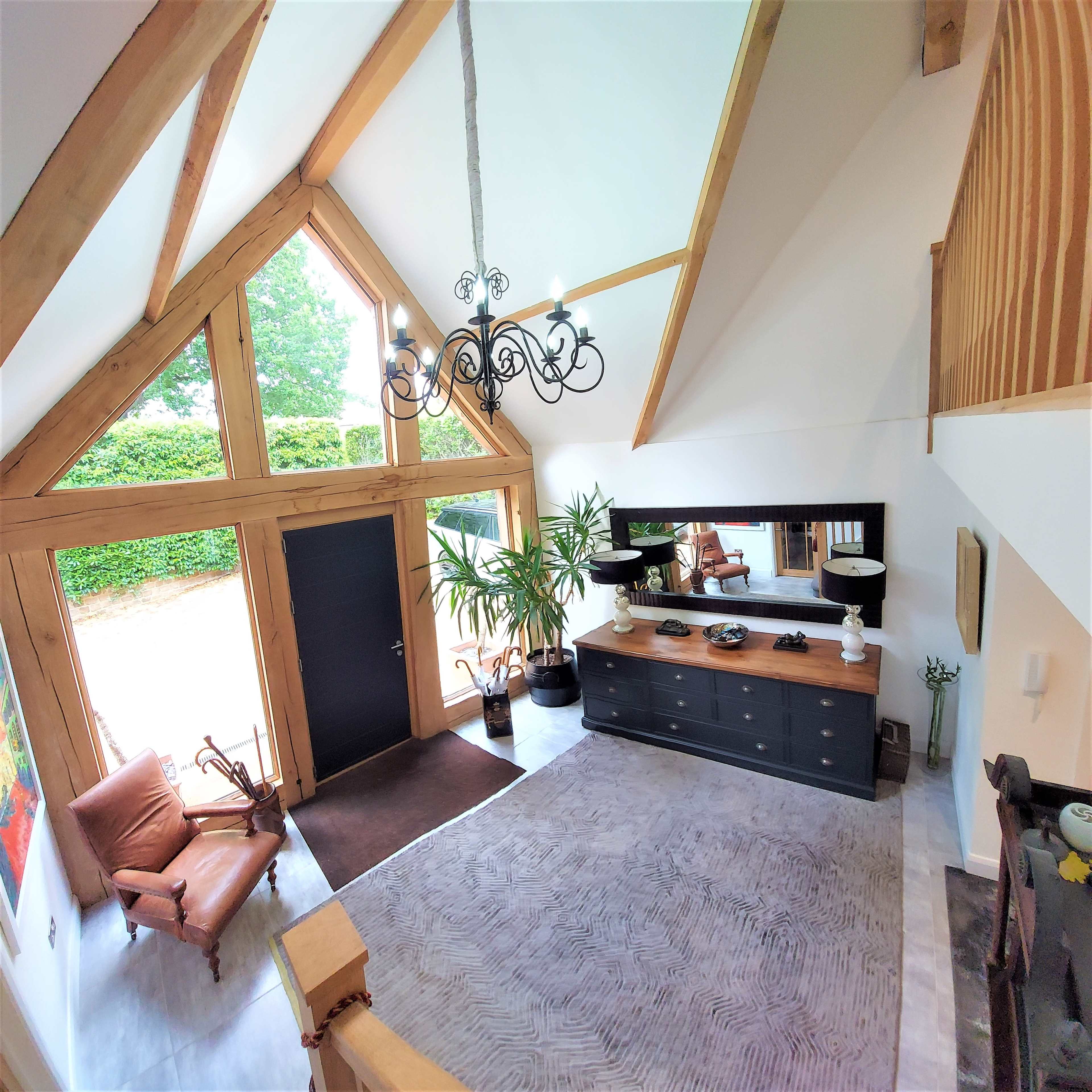 A modern entryway with high wooden beams, a large mirror, a stylish console table, and a leather armchair.
