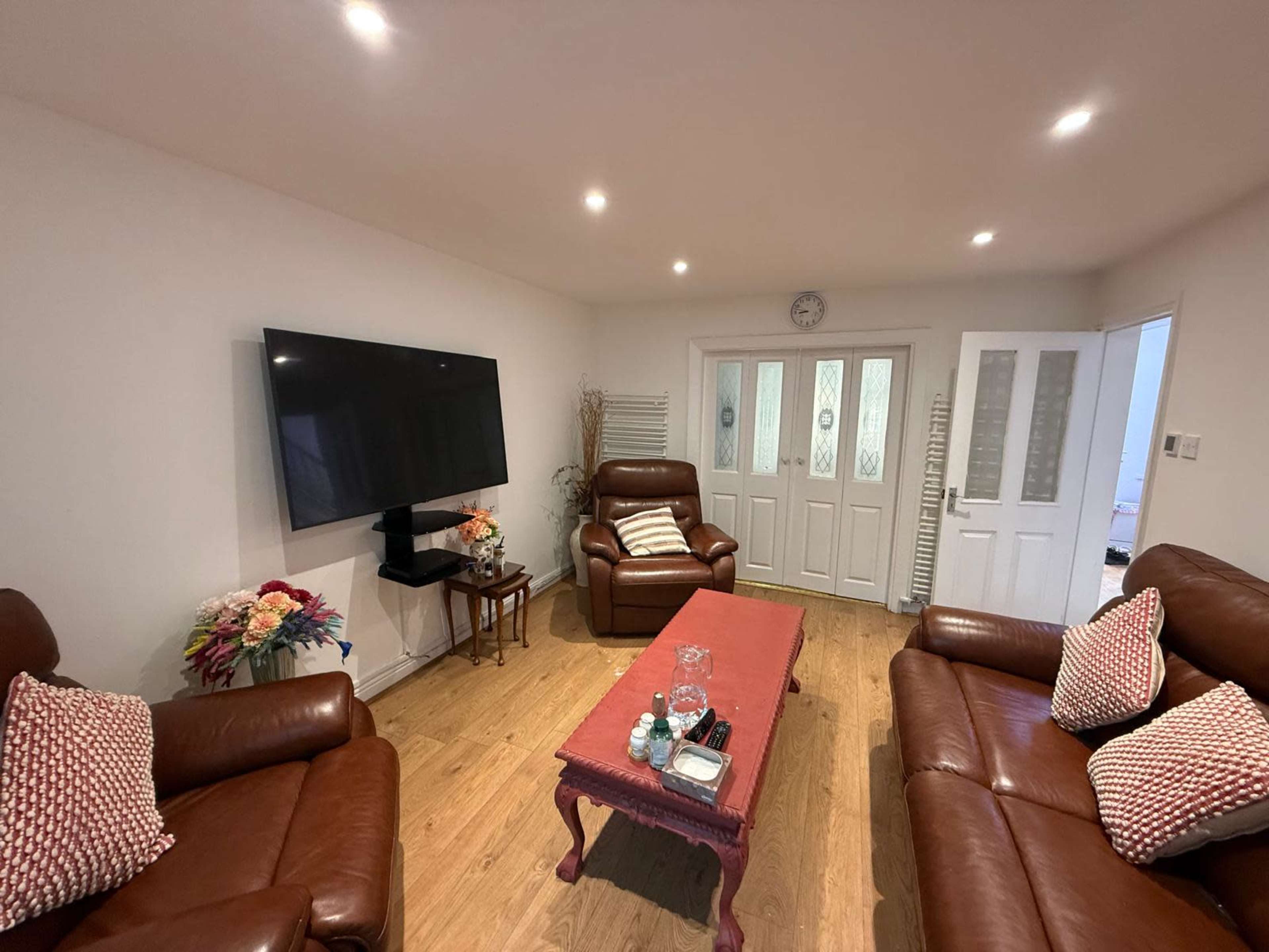 The image shows a cozy living room with two brown leather sofas, a coffee table, and a large wall-mounted TV.