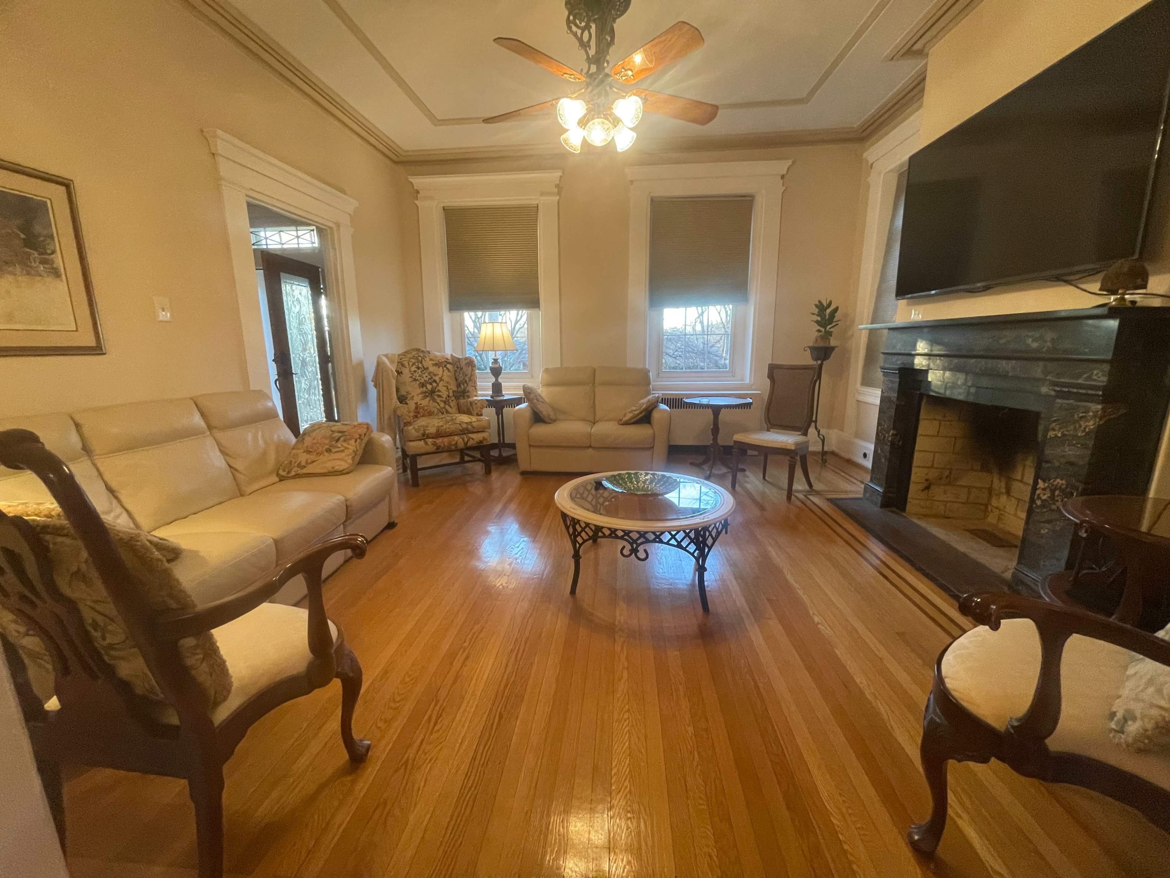 A living room with hardwood floors, a circular table at the center, and seating arranged around a fireplace.