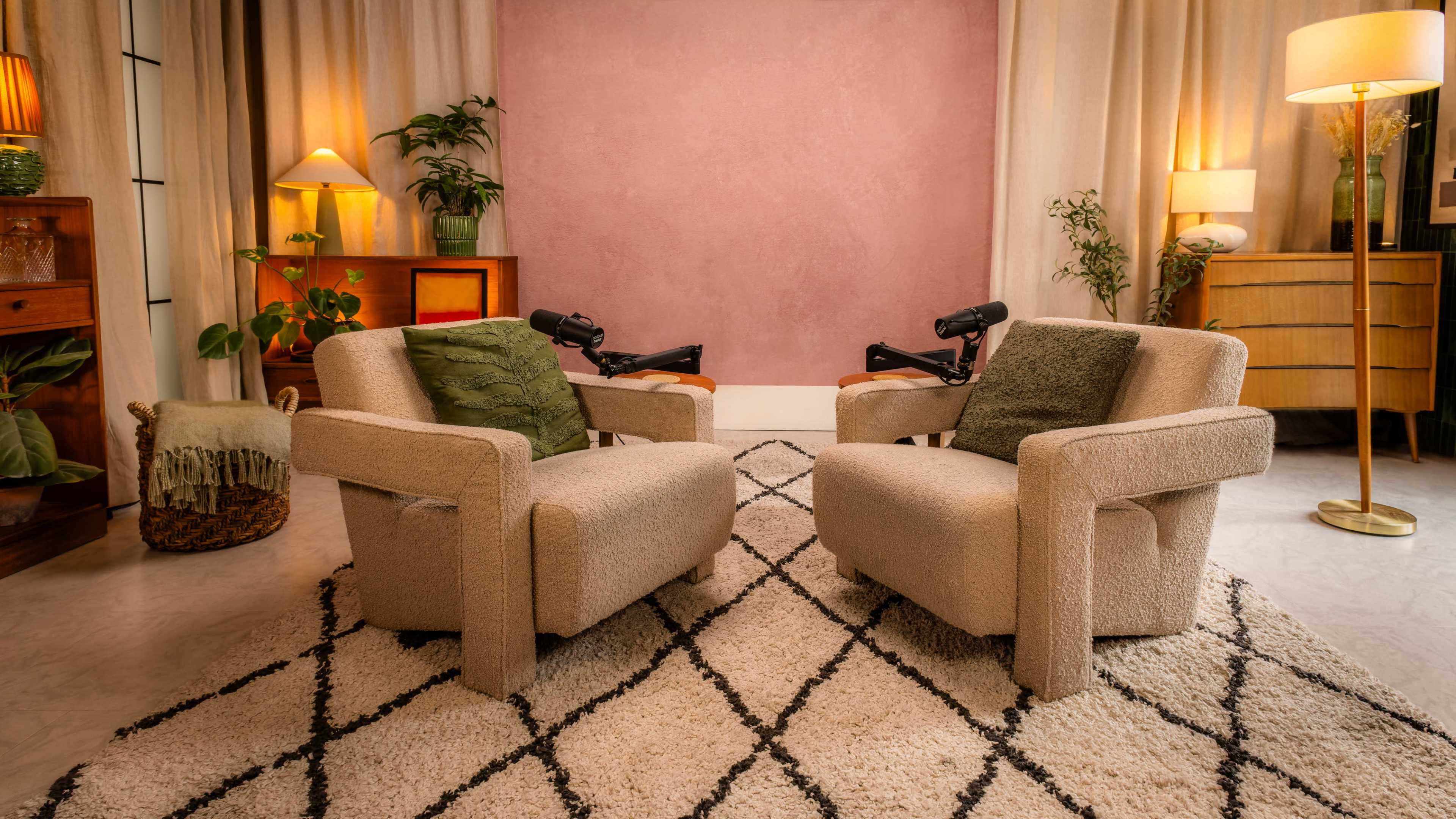 The image features two beige armchairs facing each other on a patterned rug in a warmly lit room with plants and decorative lamps.