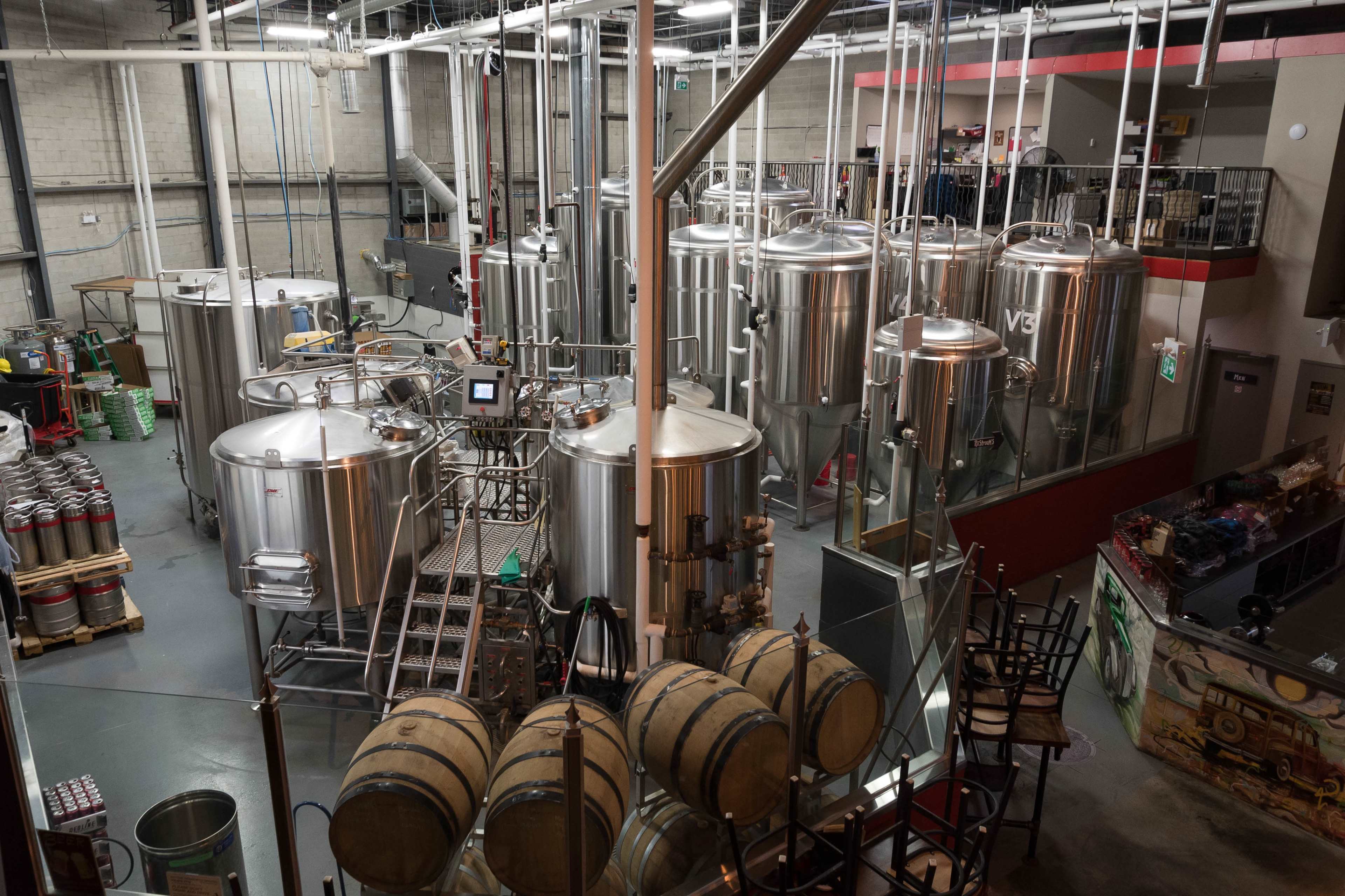 A brewery with stainless steel fermentation tanks and wooden barrels arranged in a spacious, industrial setting.