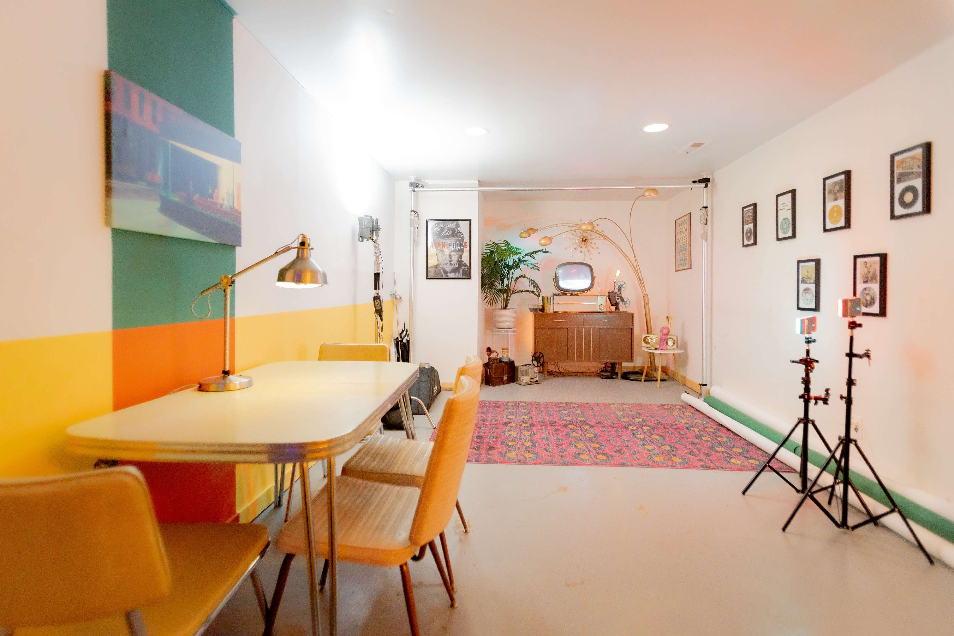 A room with a colorful wall, a table and chairs, and a vintage television set, along with framed pictures and decorative items.