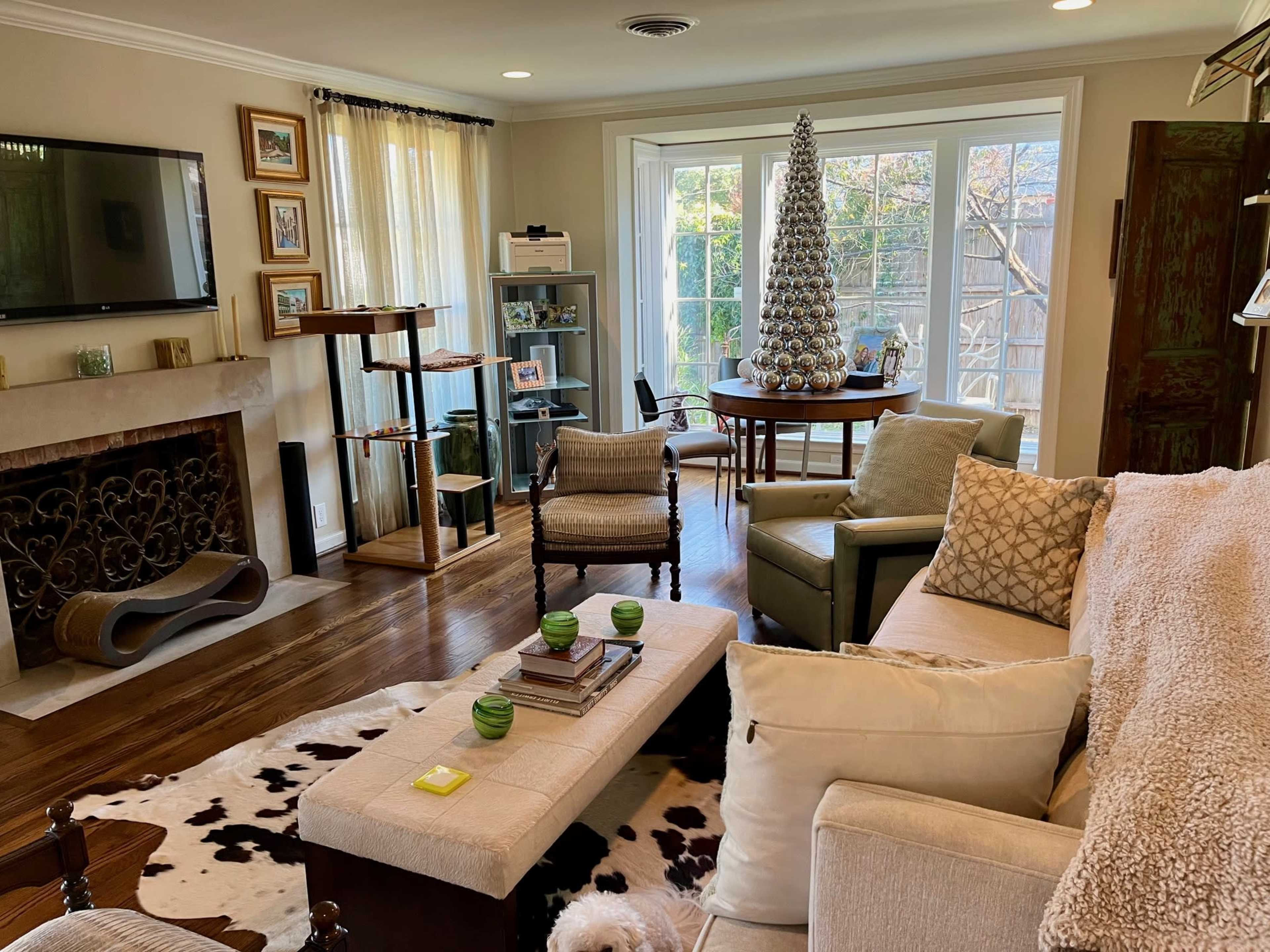 A living room features a variety of furniture including a sofa, chairs, and a coffee table, with a Christmas tree in the corner and large windows providing natural light.