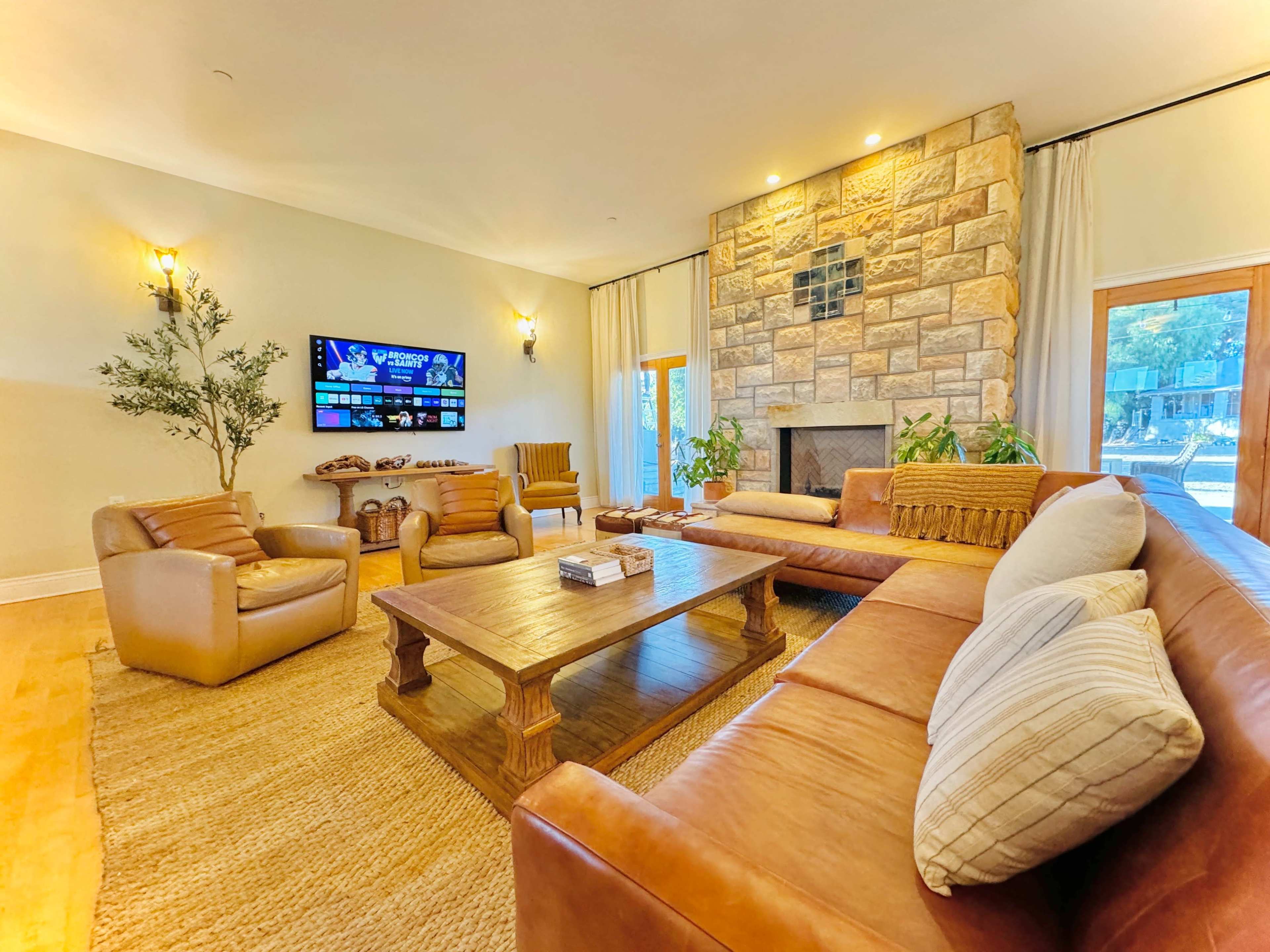 The living room features a large stone fireplace, a sectional leather sofa, wooden coffee table, and a TV mounted on the wall.