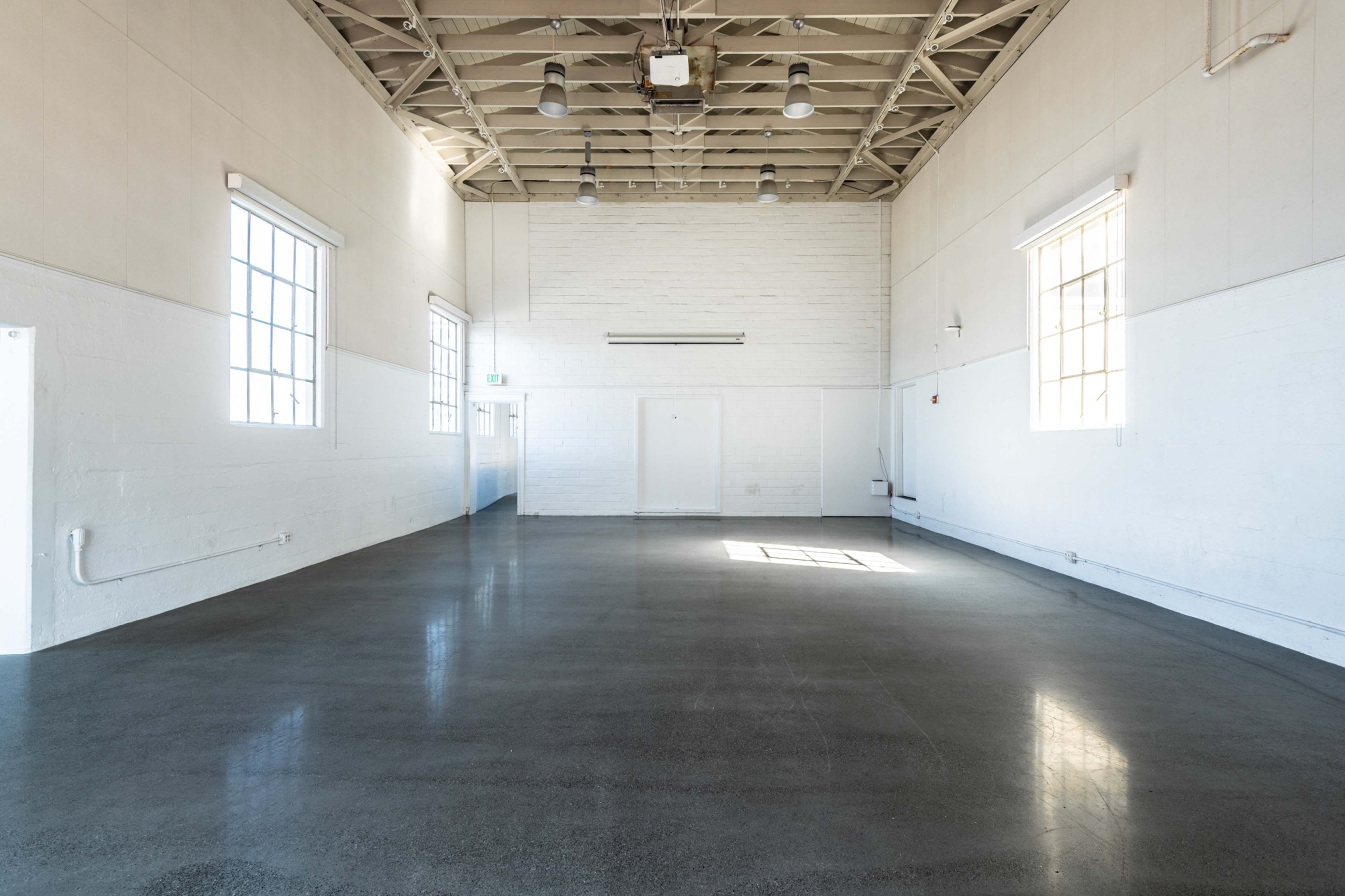 A spacious, empty room with high ceilings, large windows, and polished concrete flooring.
