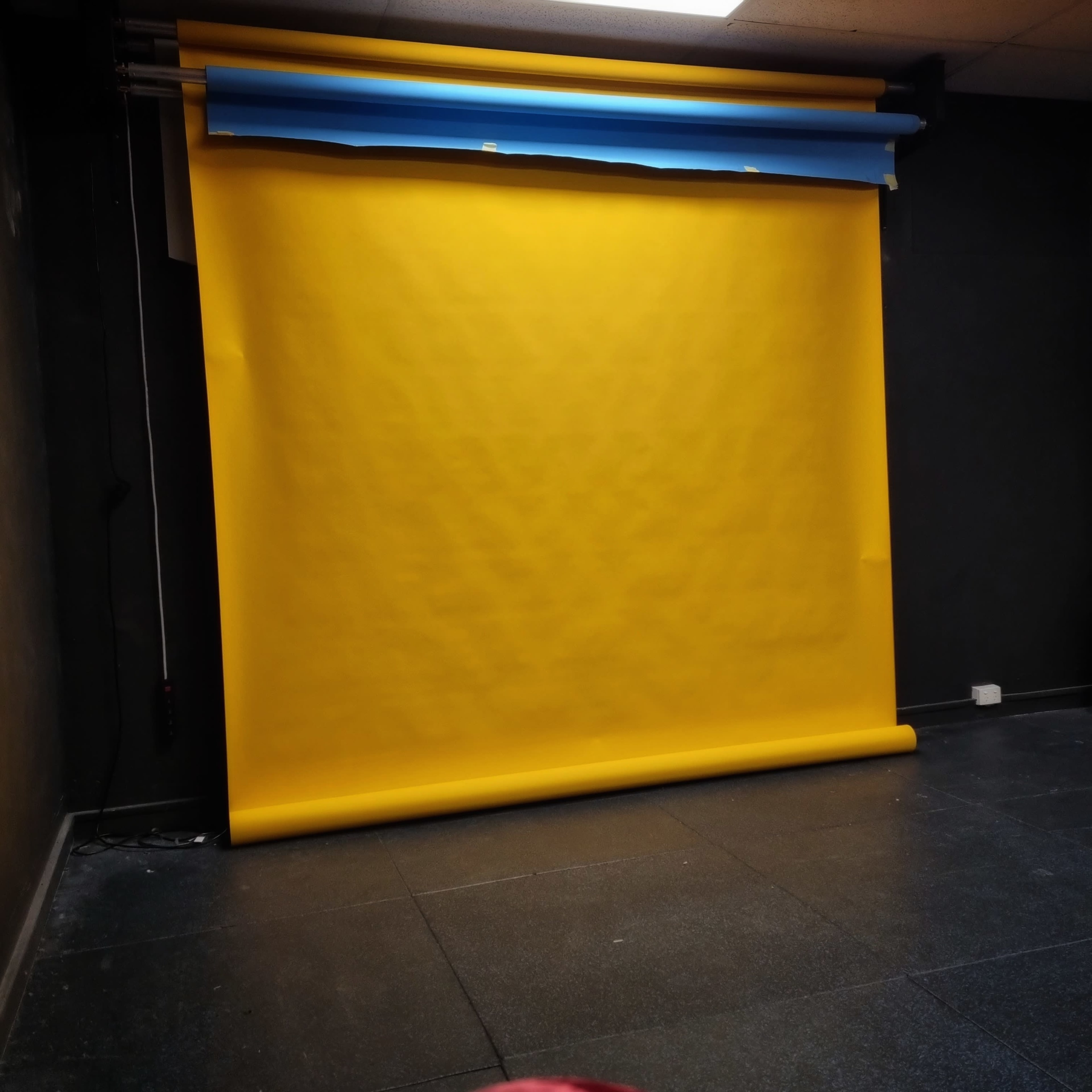 A yellow backdrop rolled down against a dark wall in a studio setting, with an upper strip of blue paper.
