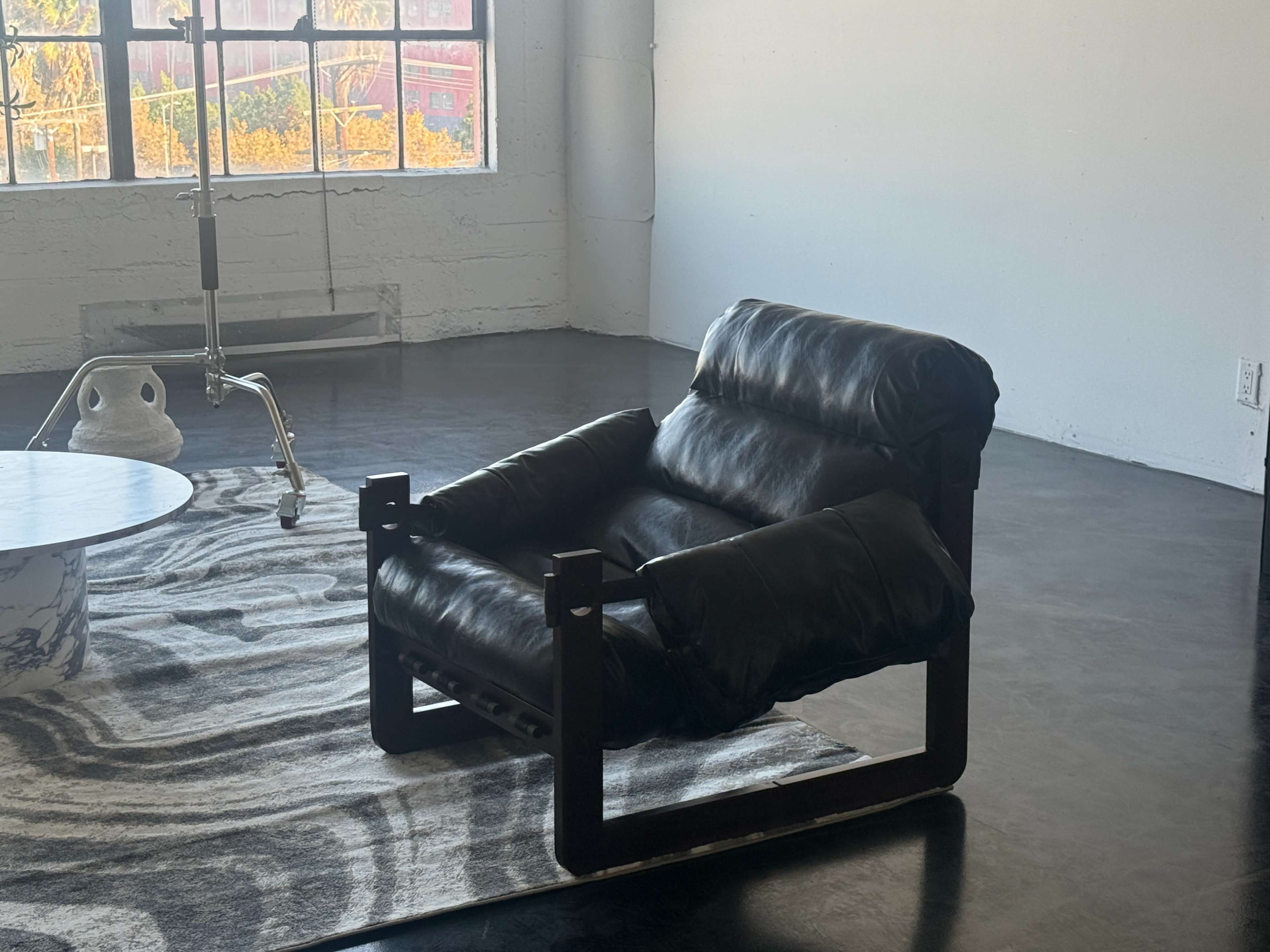 A black leather armchair with a wooden frame sits on a patterned rug in a bright, spacious room.