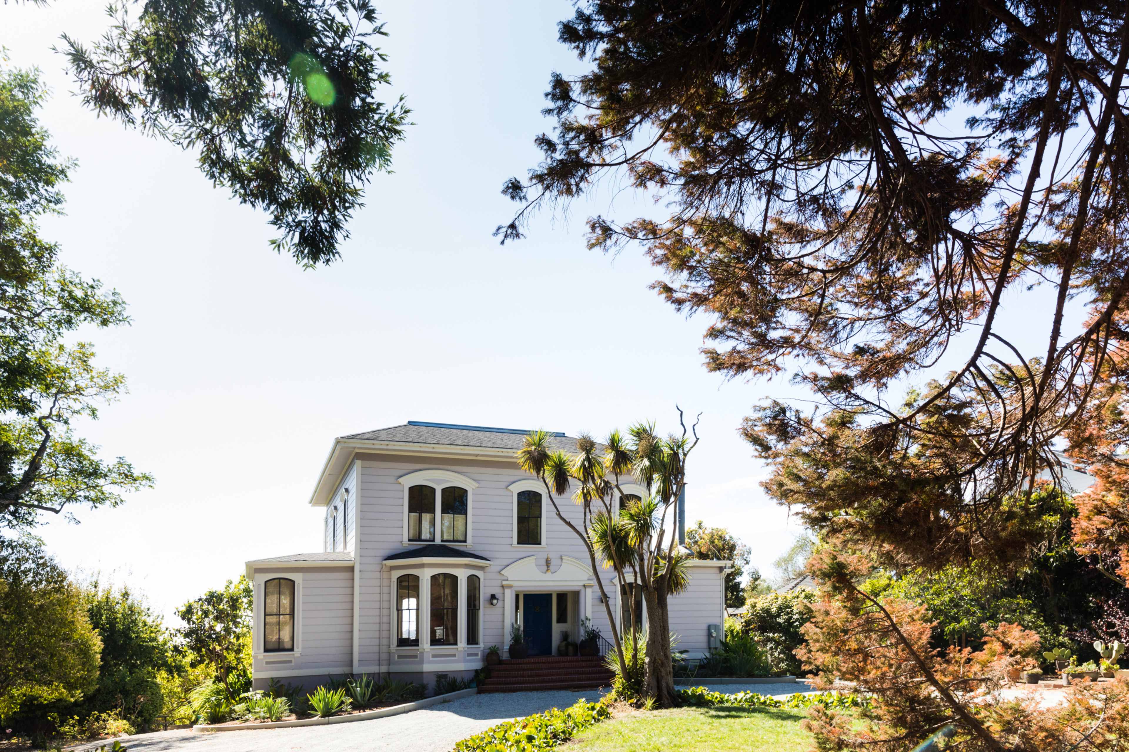 A two-story house with large windows and a landscaped front yard is surrounded by trees.