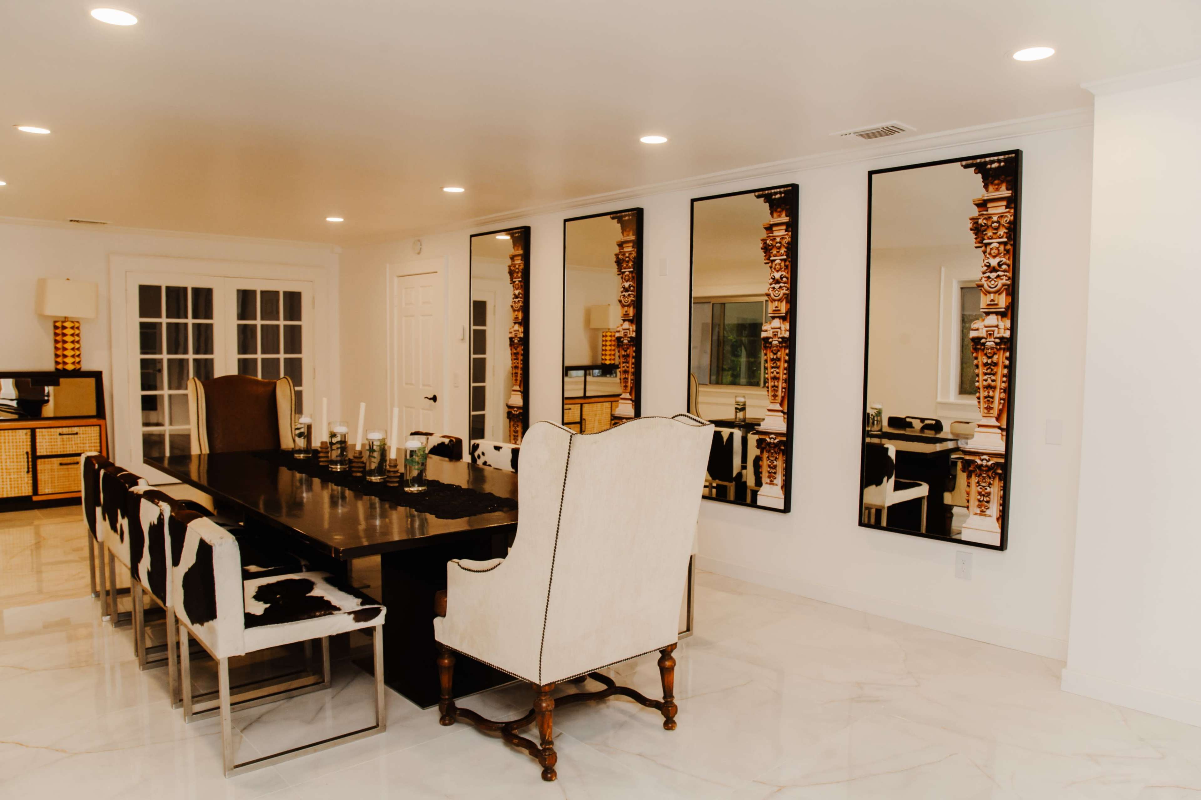 The dining room features a long black table surrounded by patterned chairs and large mirrors on the wall reflecting the space.