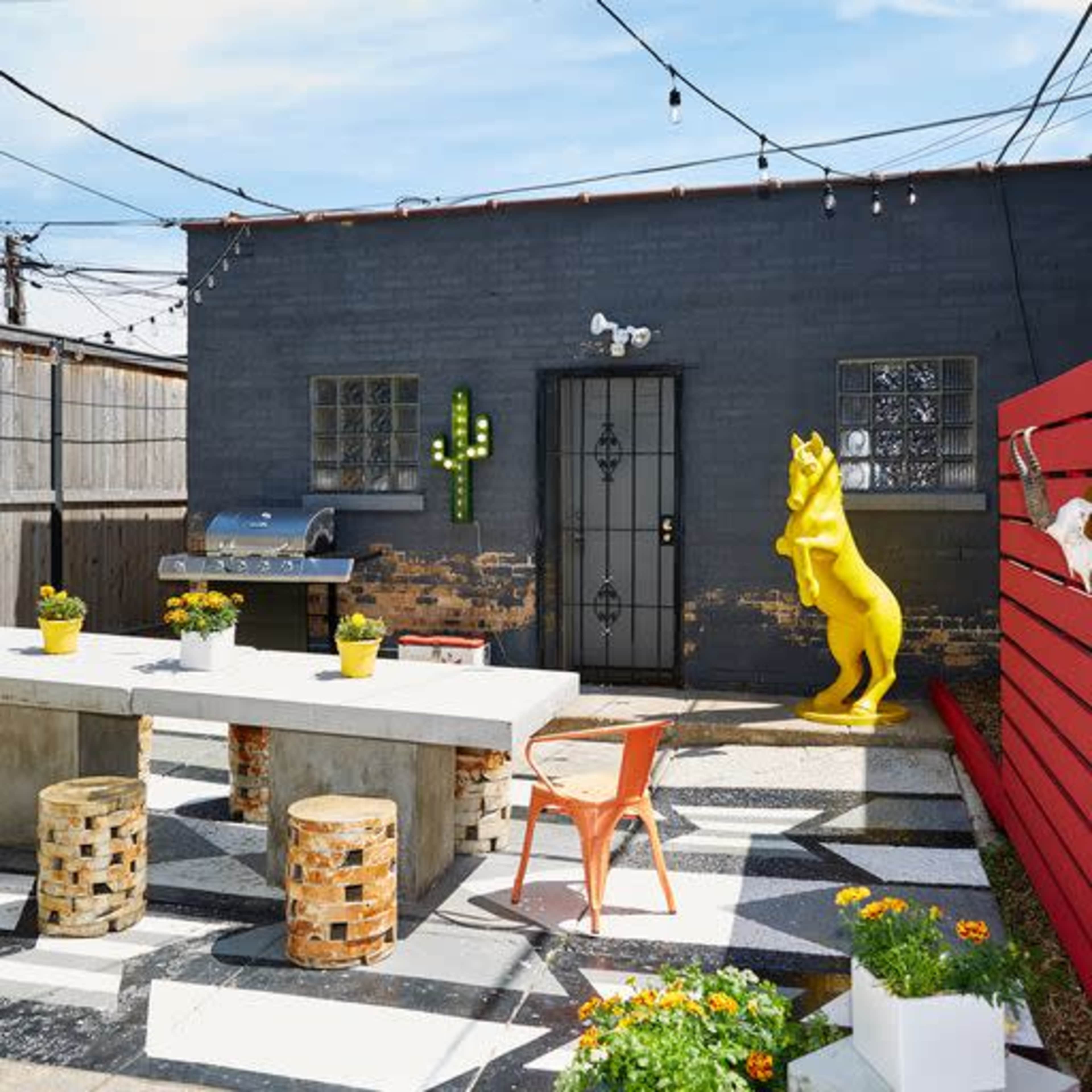 A small outdoor seating area features a white table, colorful chairs, and a large yellow horse statue against a gray wall.