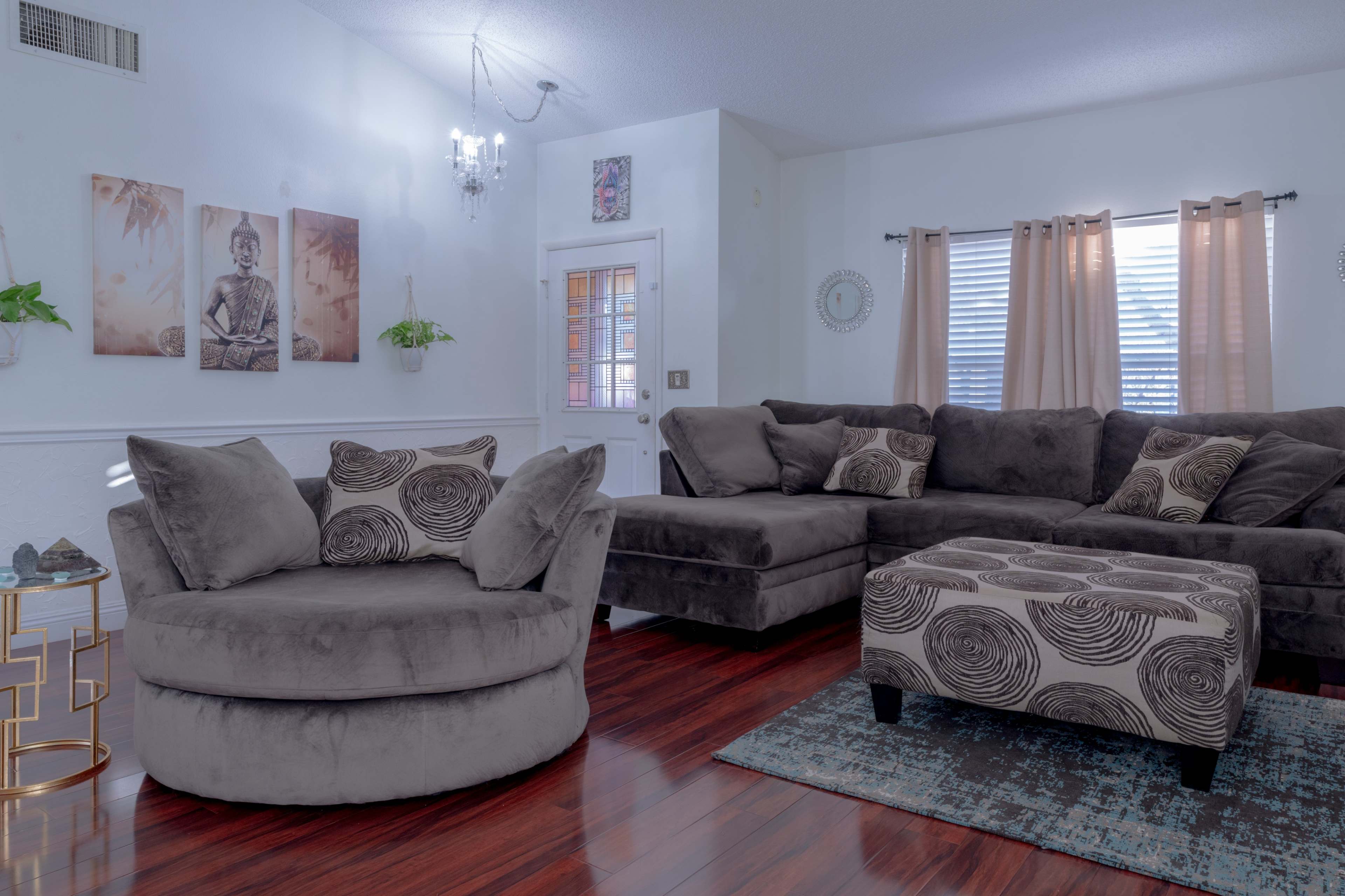 The living room features a circular gray sofa and a sectional couch, accompanied by decorative artworks and indoor plants.